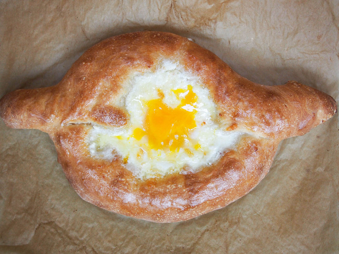 If you've not heard of adjaruli khachapuri, let me sum it up in a few words: fresh bread, filled with cheese and an egg on top. This comforting Georgian cheese bread is sure to be an instant hit (and is easier than you might think). whole Adjaruli khachapuri Georgian cheese bread from overhead