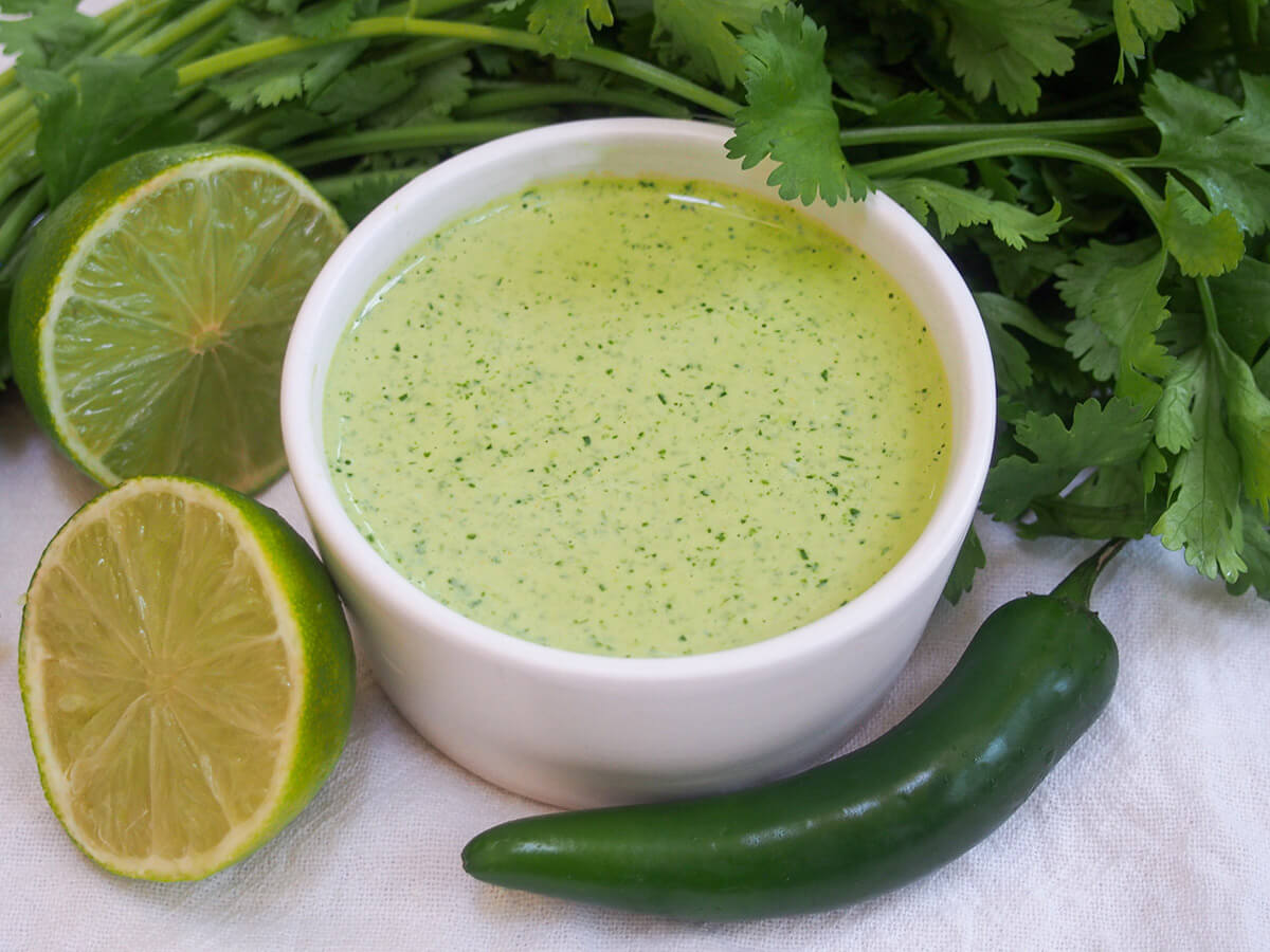 Aji verde, often called Peruvian green sauce elsewhere, is wonderfully easy and flavorful. It gets it's color from cilantro and has a little kick from aji amarillo, a popular Peruvian chili. So good. dish of aji verde Peruvian green sauce with cut lime to side and chili in front