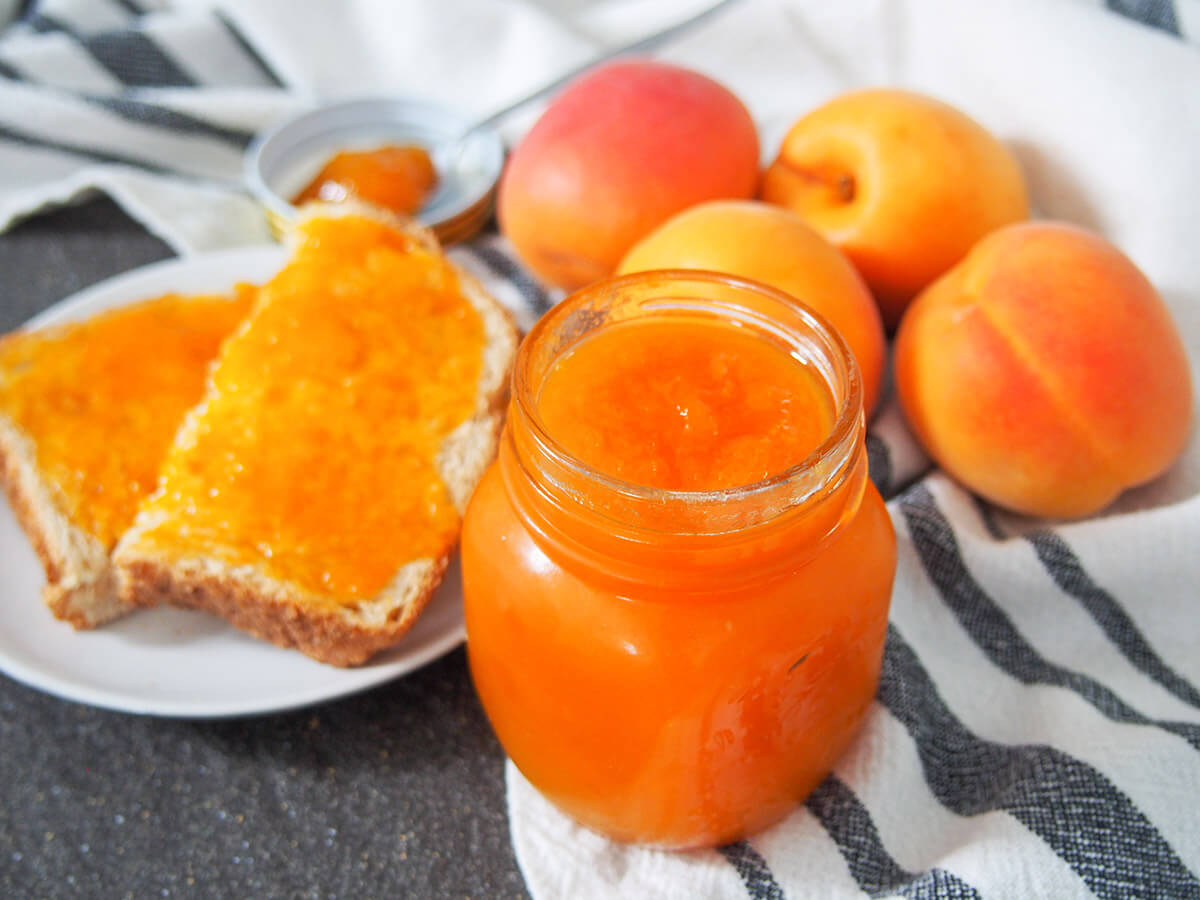 Apricot jam has such a wonderful bright color and the flavor is equally irresistible. It's smooth, almost aromatic and the perfect addition to toast and so much more. This version is lower sugar, too. jar of apricot jam with bread and jam and fresh apricots behind jar