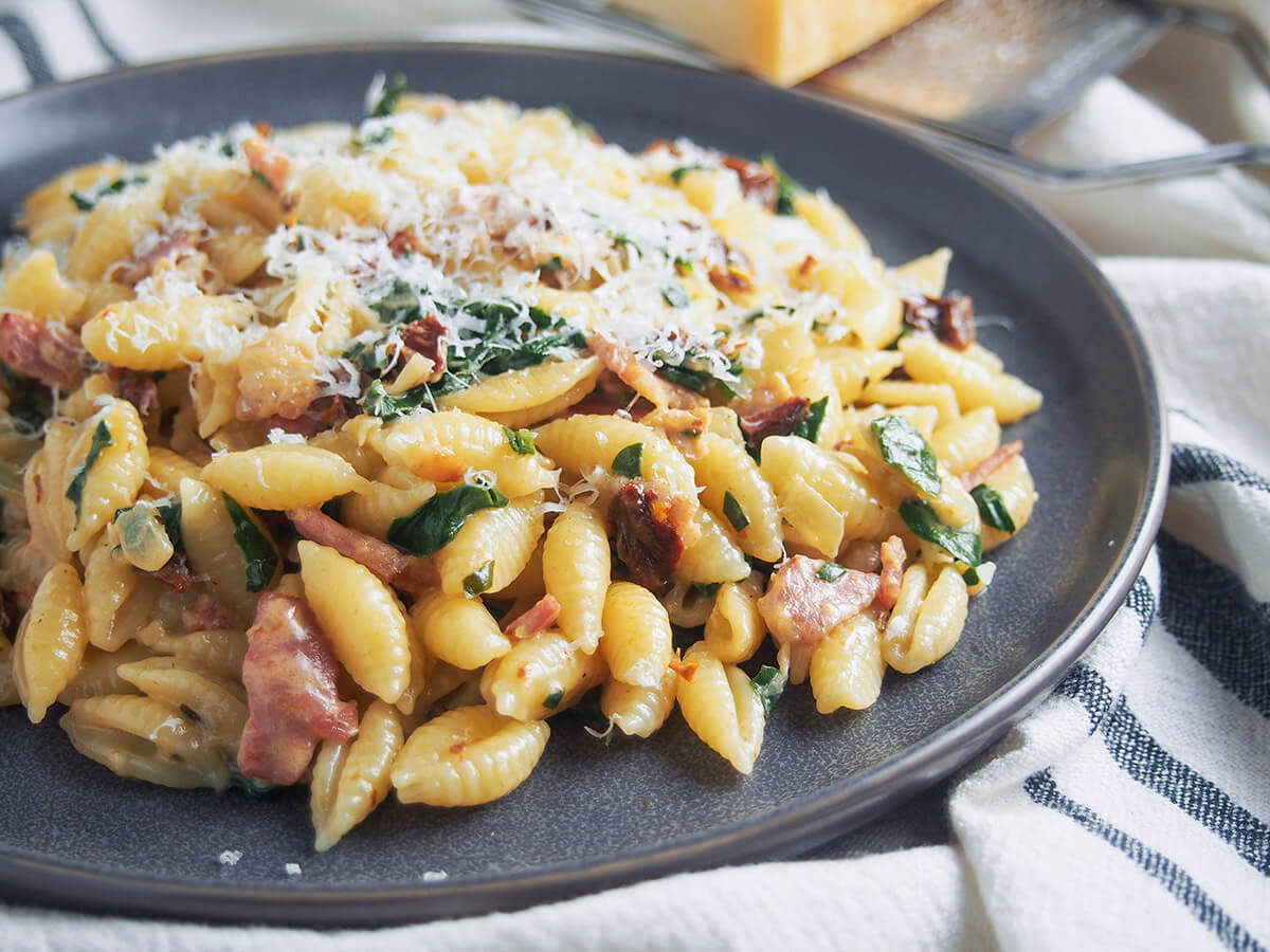 This bacon sun dried tomato pasta with spinach and cream is quick to make and full of delicious flavors that all will enjoy. Comforting and just that bit different, it's a great easy meal. side view of plate of Bacon sun dried tomato pasta with spinach and cream
