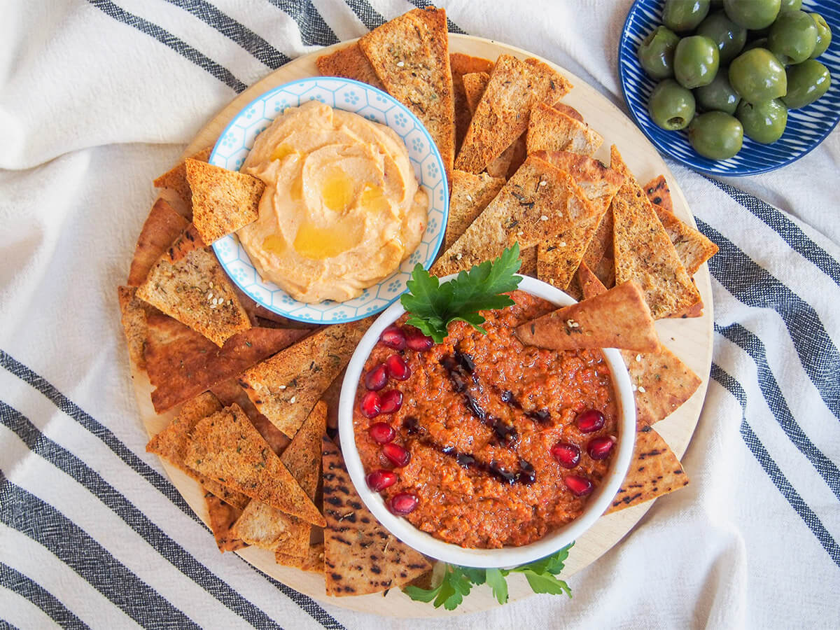 These baked pita chips are gently seasoned, have a fantastic crunch and are really quick and easy to make, too. Perfect to snack on as they are, and equally good for dipping. They'll be gone in no time! board with baked pita chips, two bowls of dips and olive to side