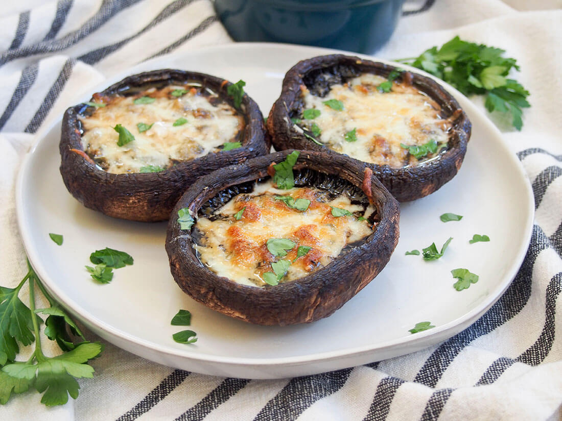 These baked portobello mushrooms are easy to prepare and packed with delicious cheese and garlicy goodness. Meaty enough to satisfy any carnivore, and versatile enough to work as a main or side. plate of three baked portobello mushrooms topped with cheese and a little parsley on top