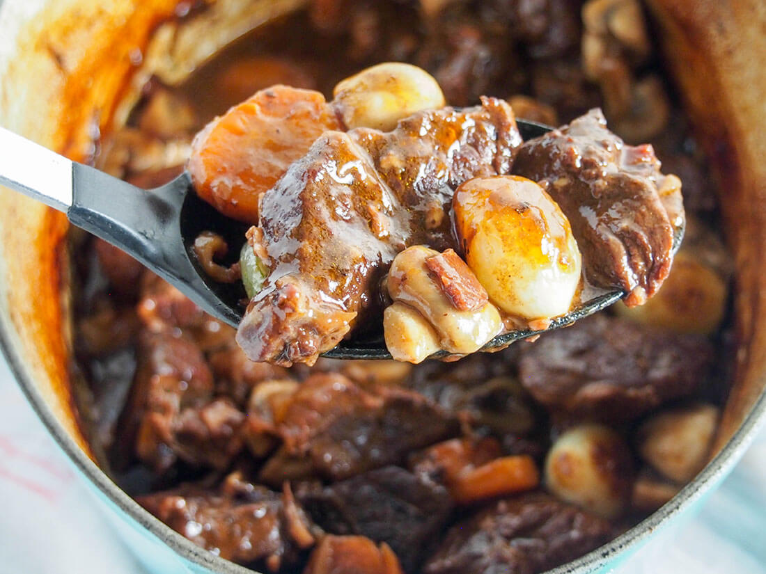 Beef bourguignon may not be the quickest meal to make, but it's time very well spent. And with this easy recipe, you'll see exactly how to get perfectly tender, flavorful beef and a mushroom, bacon and red wine gravy to die for! Beef bourguignon with spoonful held in front of pot holding rest