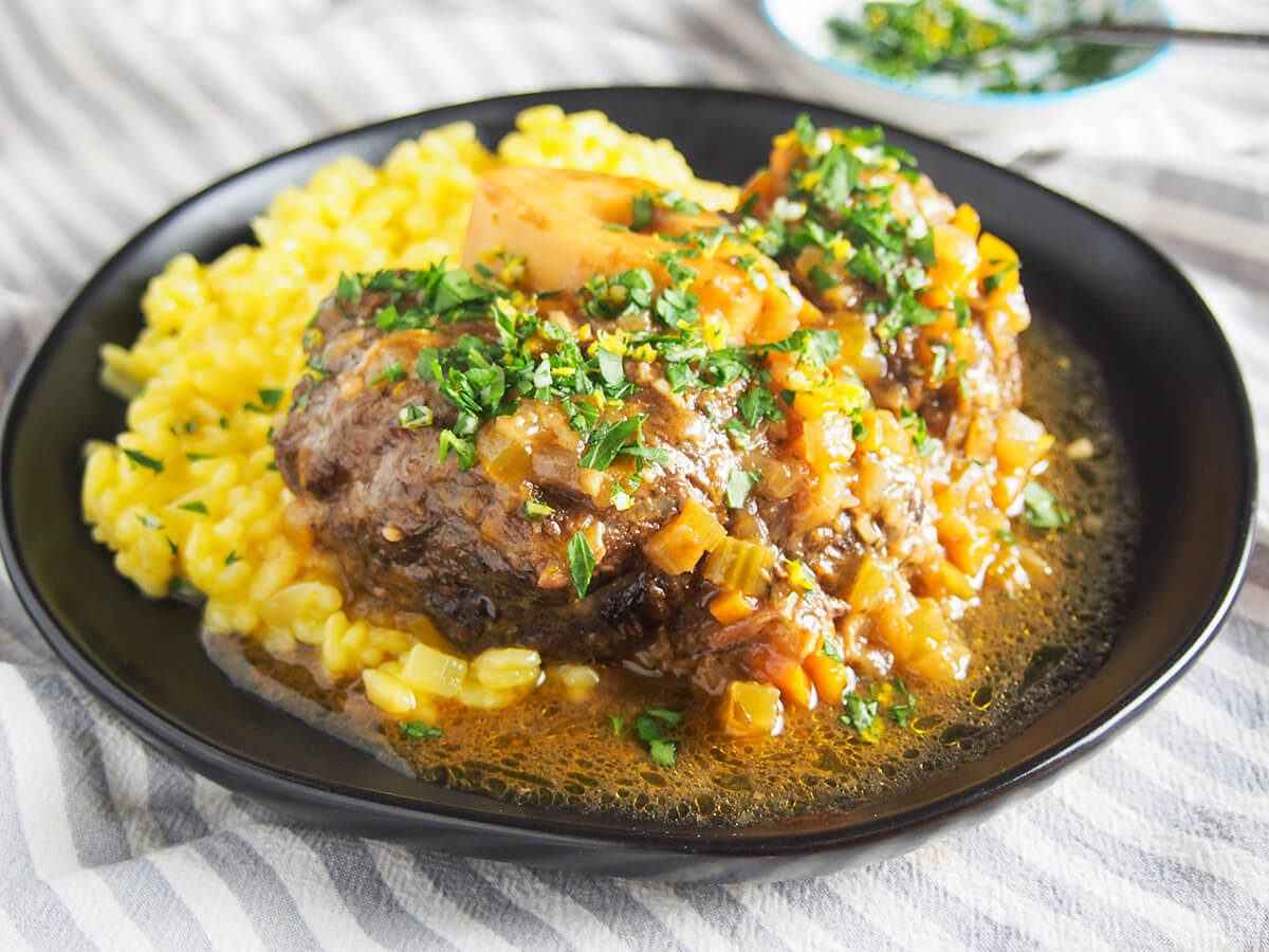 Osso buco is a traditional slow cooked Italian dish. Traditionally made with veal, this beef version has the same delicious meltingly tender meat and bright gremolata finish. Perfect comfort food. plate of beef osso buco on top of saffron risotto