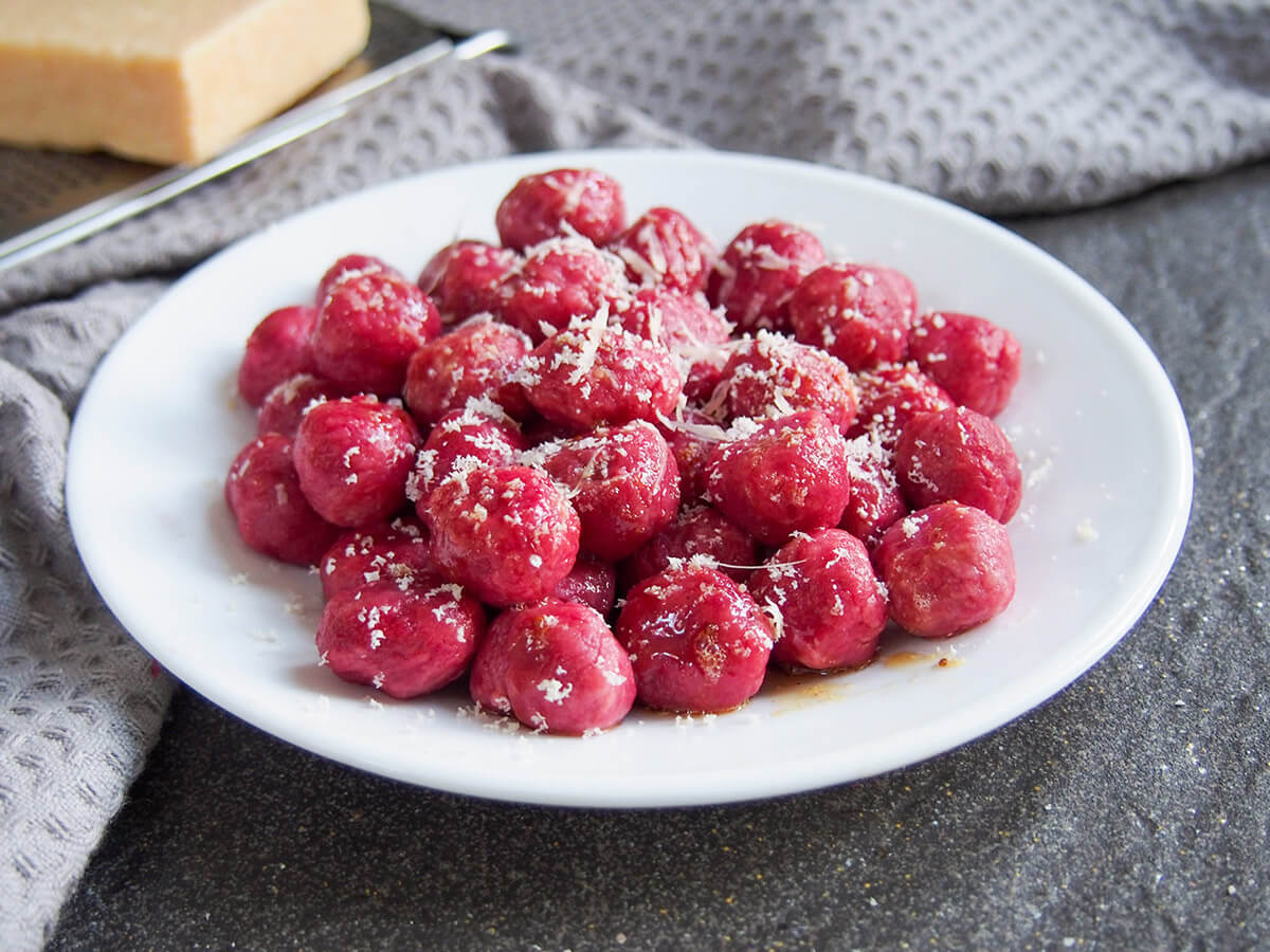 These beautifully colored beet gnocchi are as delicious as they are pretty. They have a mild flavor with a light creaminess from the ricotta in them. Perfect to brighten up your plate. plate of beet gnocchi with cheese to side