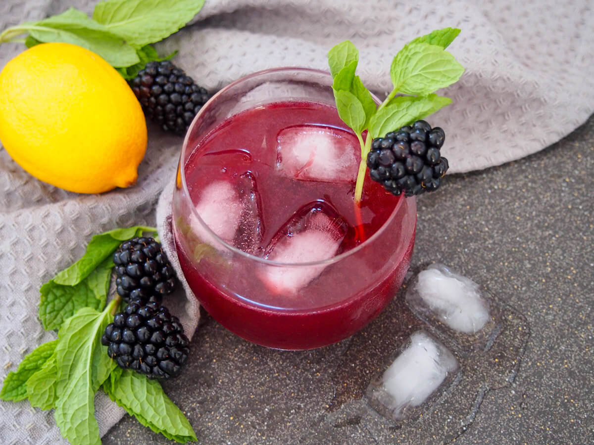 This blackberry bourbon smash is as bright and bold in flavor as it is in color. It's easy to make, relatively strong but deliciously smooth & gently refreshing. glass of blackberry bourbon smash with lemon, blackberries and mint to side