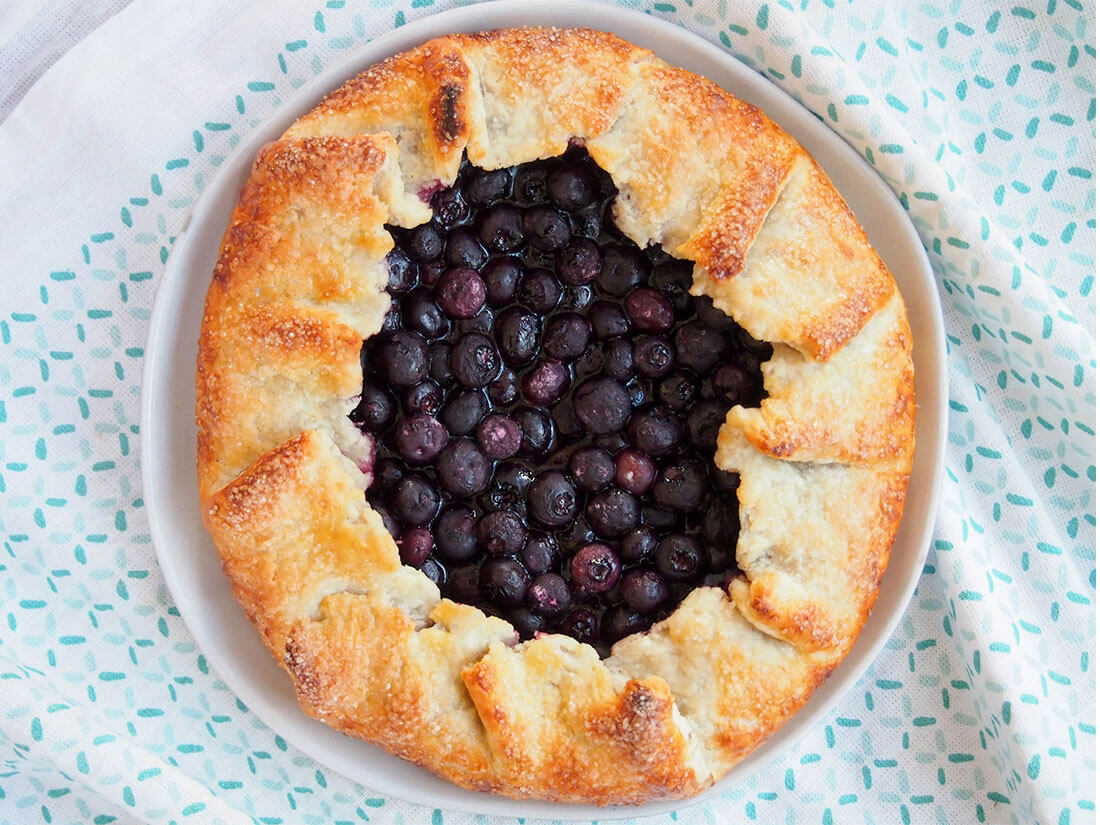 Don't think the name blueberry galette means this is fancy or difficult. This rustic free form tart is easy to make and so delicious. Crisp, tasty and oozing with berries. whole blueberry galette on plate