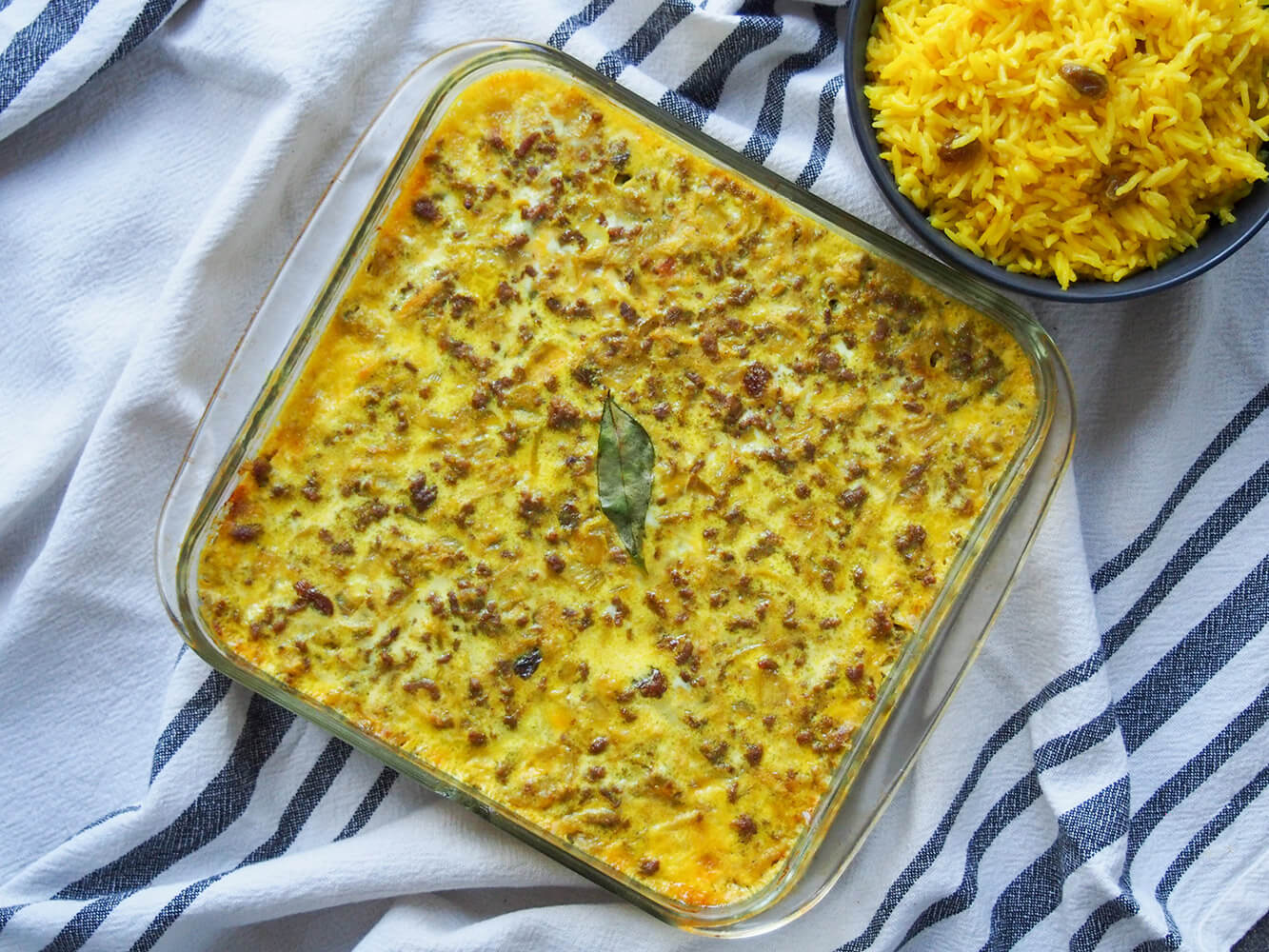 Often considered the national dish of South Africa, bobotie is a fantastic mix of flavors, with fruit, curry and spice in a comforting meaty bake. whole bobotie in baking dish with rice to side