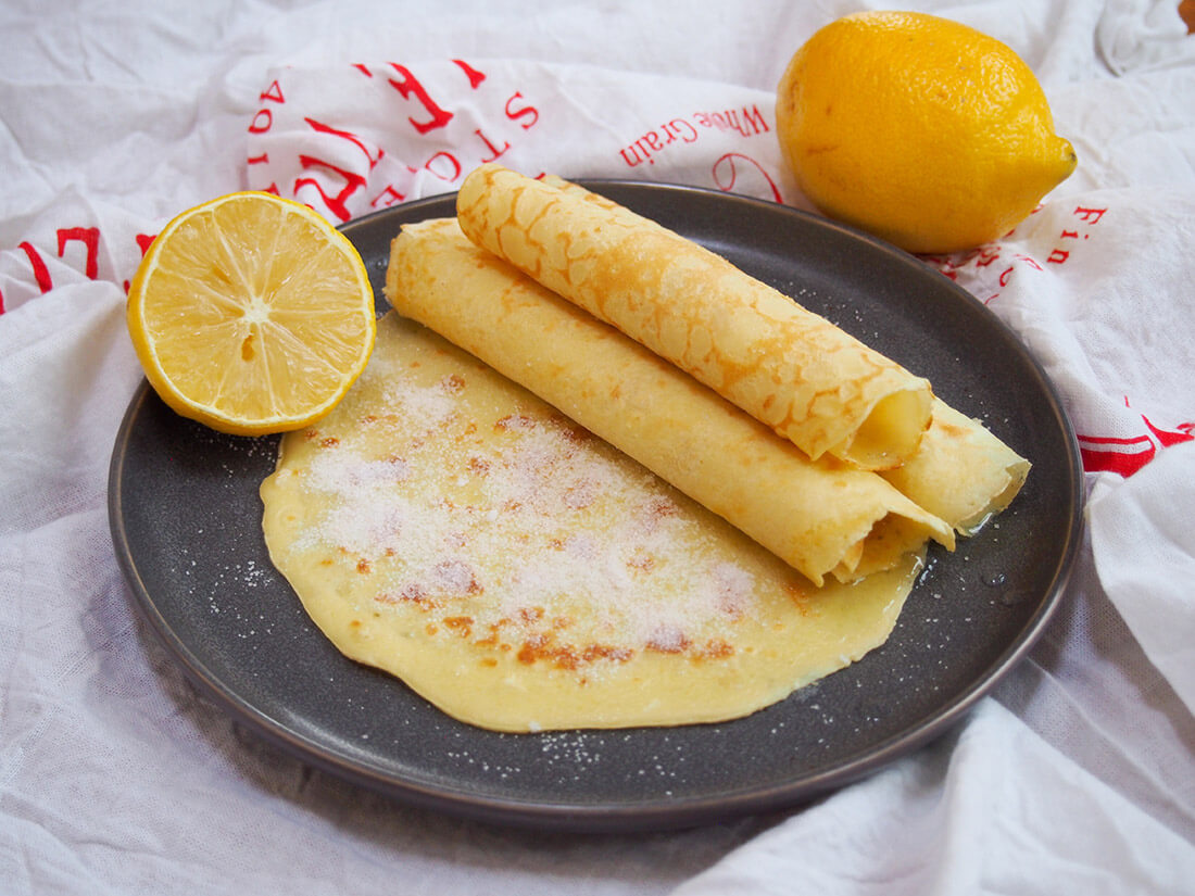 These British pancakes are easy to make with only a few ingredients. While they're traditional for Shrove Tuesday (Mardi Gras), they make a delicious snack or dessert any time. British pancakes rolled in small stack with lemon to side
