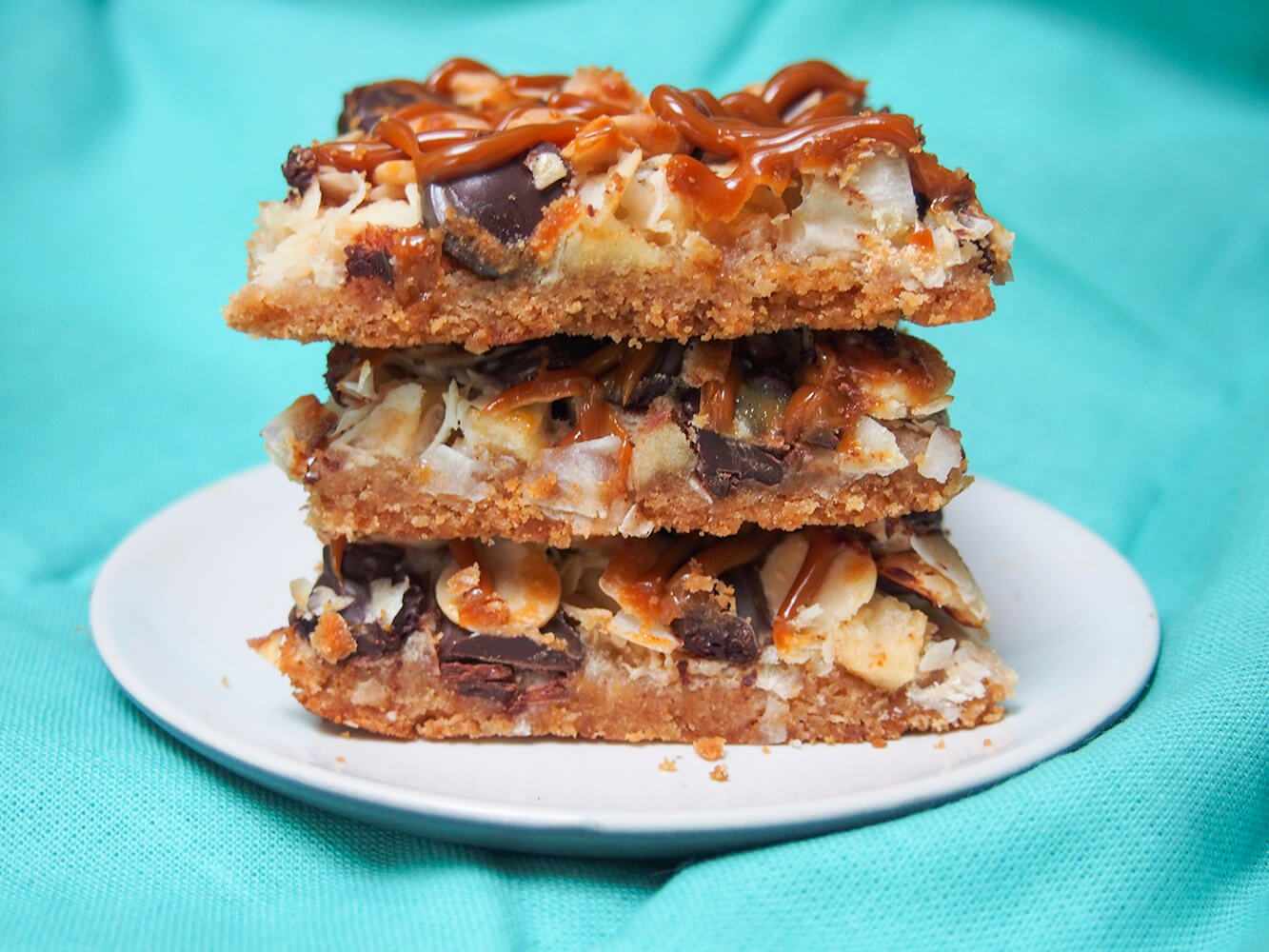 These caramel apple magic bars take the classic layered bars up a step with chunks of apple and a caramel drizzle. caramel apple magic bars in stack on plate