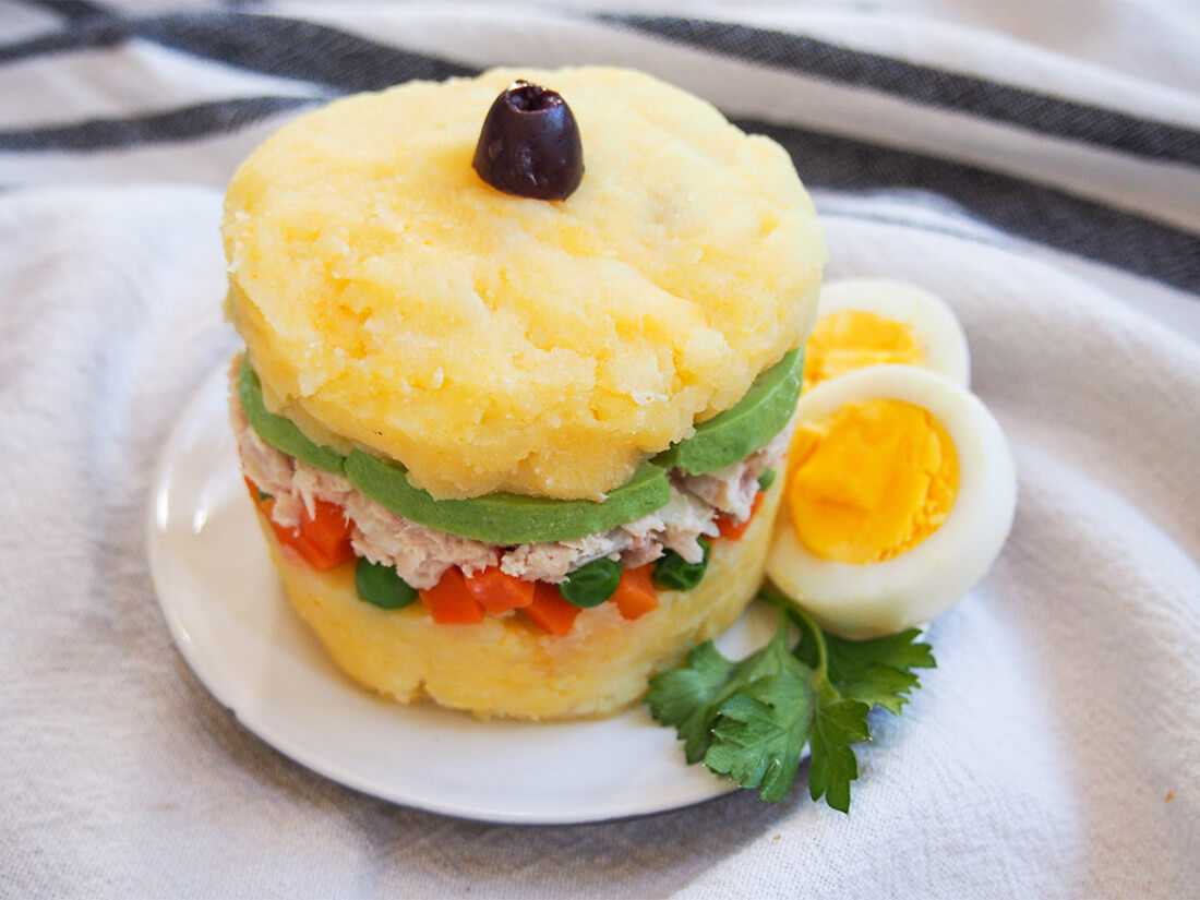Causa rellena is a classic Peruvian appetizer that takes simple ingredients and transforms them into something elegant and delicious. This pretty layered stack is great for entertaining and more. Causa rellena on plate with egg garnish