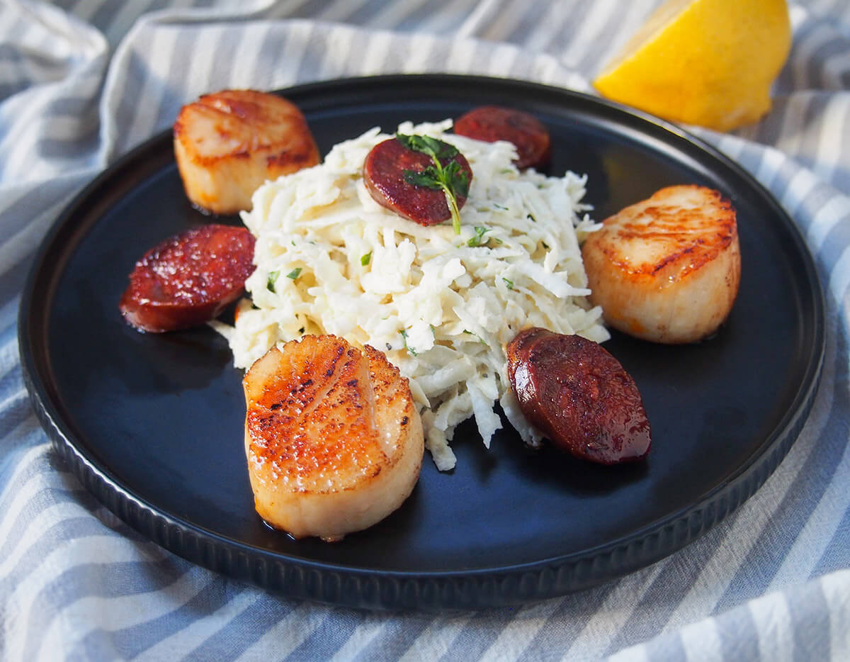 A simple celeriac remoulade pairs perfectly with pan-seared scallops. Some crisped chorizo round this out into a flavorful, elegant but quick and easy meal. plate of celeriac remoulade seared scallops and chorizo