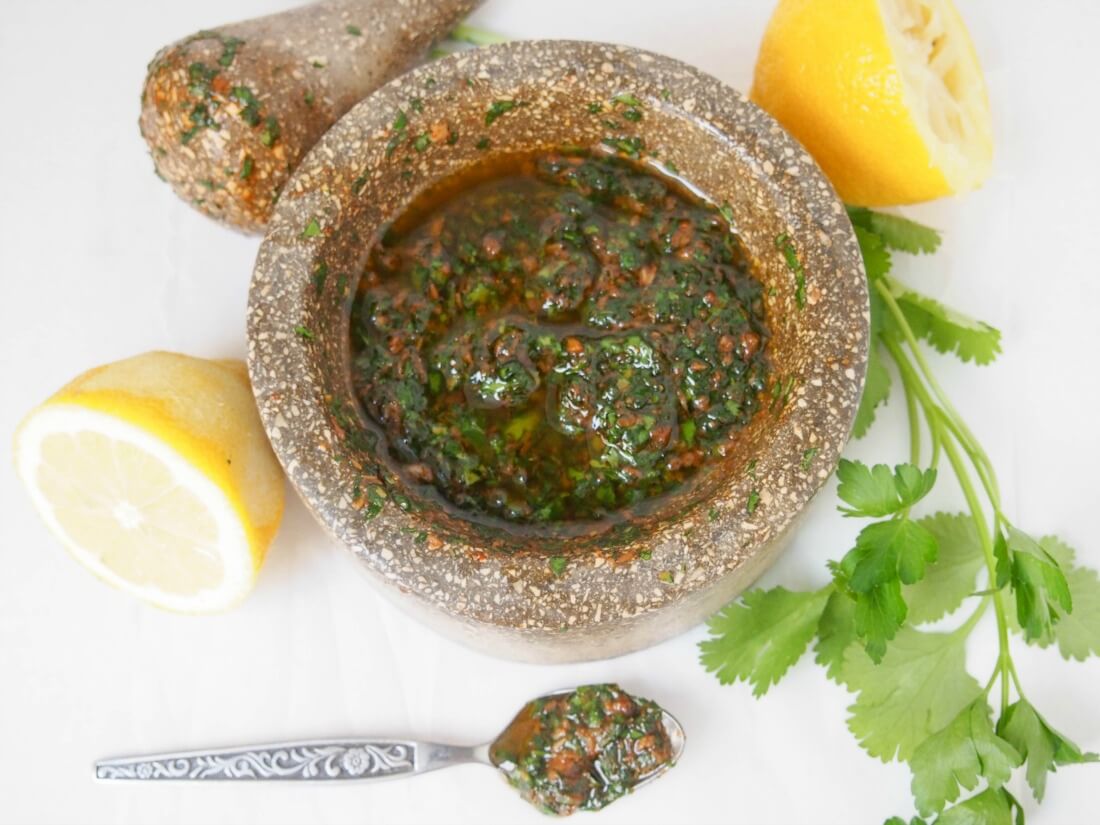 This chermoula sauce is easy to make and packs a delicious flavor punch - fresh herbs, cumin, garlic and olive oil, it's great with fish, vegetables and so much more. chermoula sauce in mortar from overhead with lemon and cilantro to side