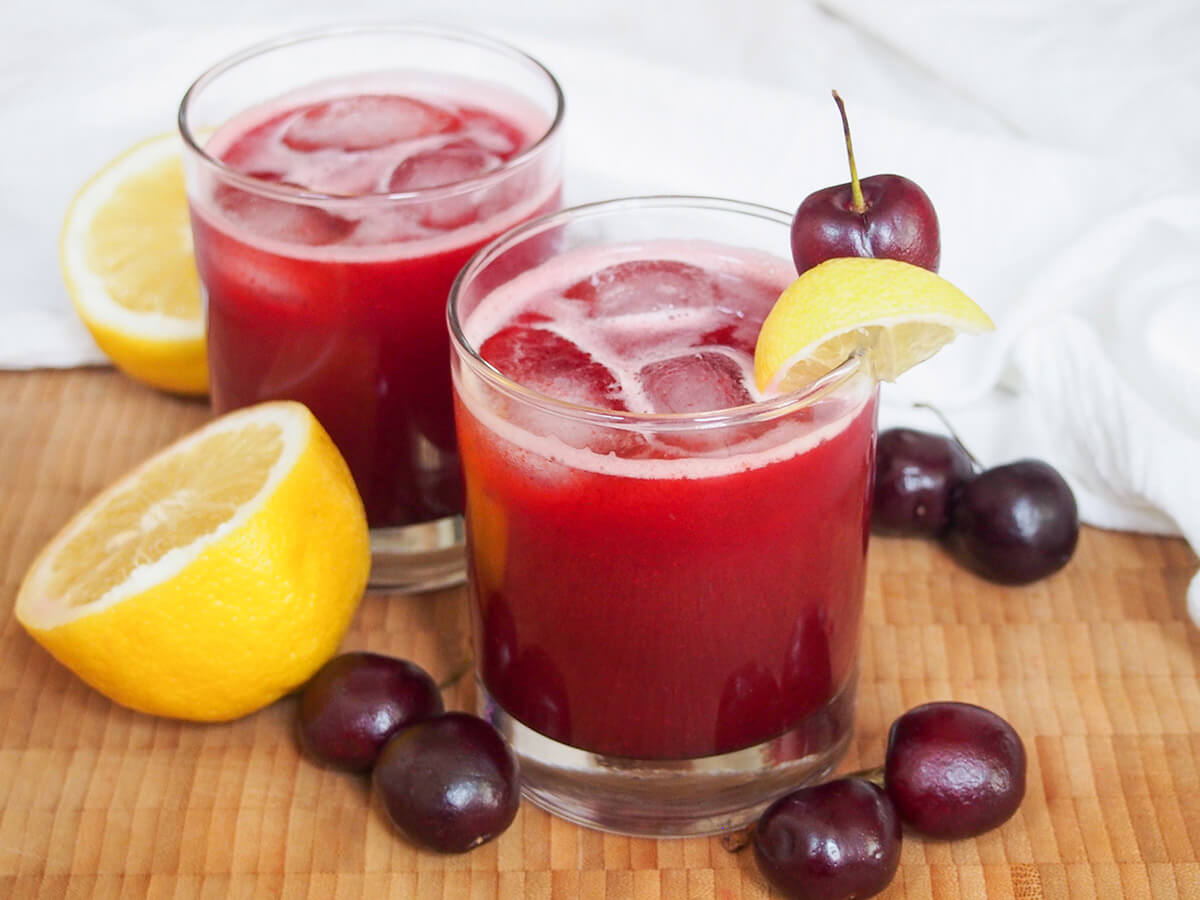 bright and refreshing cherry lemonade two glasses of cherry lemonade with lemons and cherries to either side