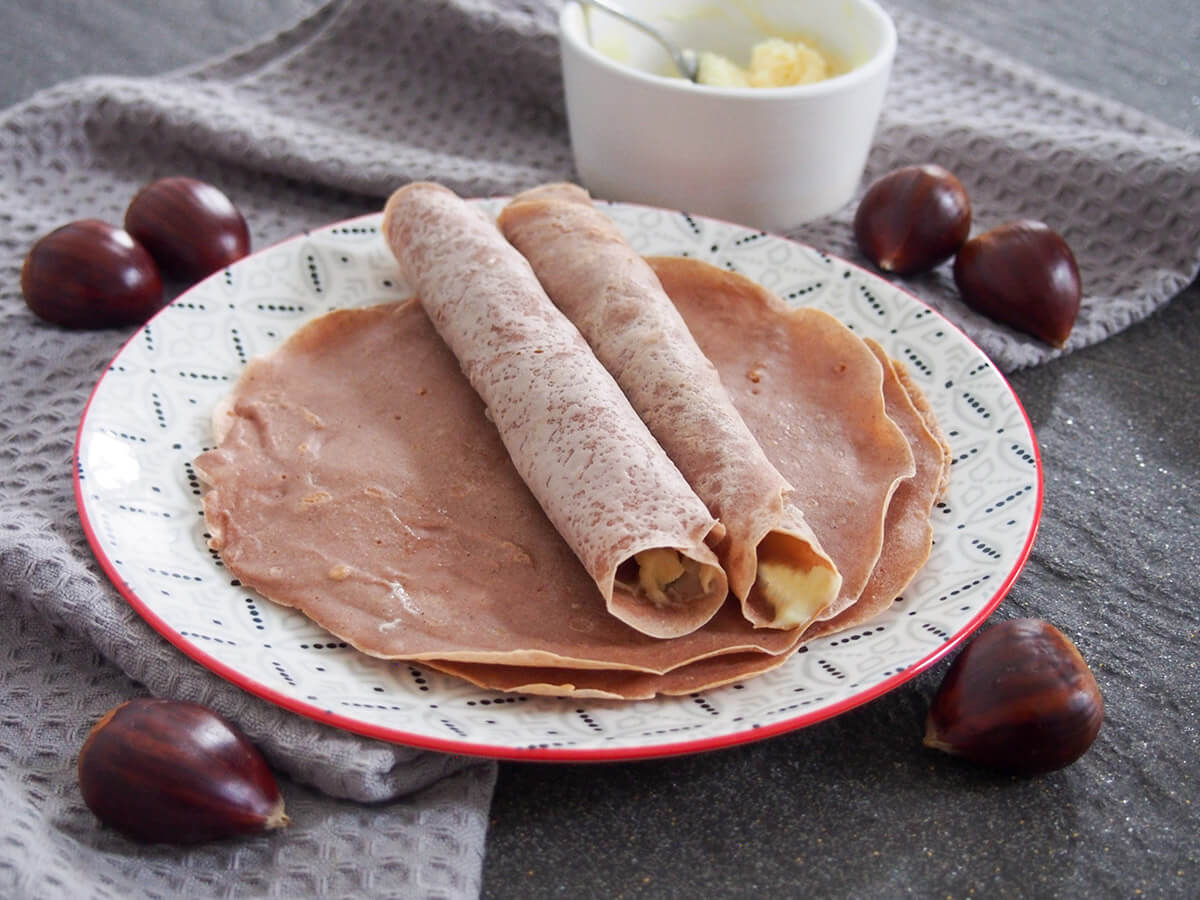 These chestnut crepes or pancakes are easy to make, naturally gluten-free and have a delicious, gently sweet nutty flavor. The sweet and creamy honey mascarpone pairs perfectly to make a tasty snack, breakfast or even dessert. two rolled up chestnut crepes on top of more on plate with chestnuts around plate