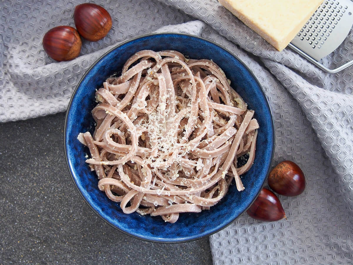 This chestnut pasta is a wonderfully tasty homemade pasta with a gently sweet, nutty flavor. It's easy to make and cooks up in no time. It pairs perfectly with simple sauces for comfort food deliciousness. bowl of chestnut pasta with whole chestnuts to side of bowl and cheese on grater above.