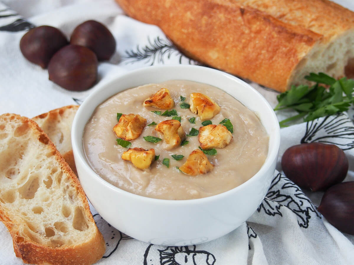 French chestnut soup (velouté de châtaigne) is wonderfully silky smooth, with a slightly earthy, nutty flavor. It's really easy to make and perfect for colder days. Warming, comforting and delicious. bowl of chestnut soup with slices of bread to side and chestnuts behind.