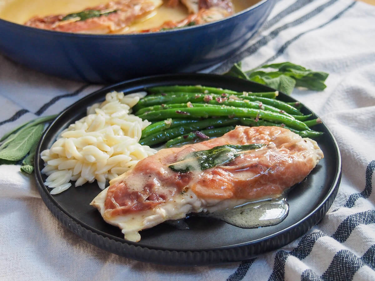 This chicken saltimbocca is a delicious chicken version of the classic Italian dish. It's packed with flavor, both in the chicken and the sauce with it, yet all easy and quick enough for a midweek meal. plate of chicken saltimbocca with green beans and orzo behind