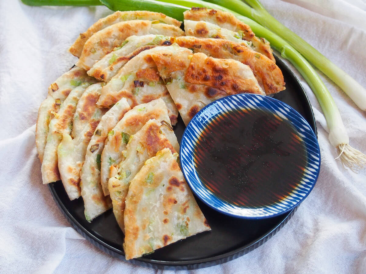 Chinese scallion pancakes are a street food and restaurant favorite. They're easier than you might think with a delicious mix of flaky layers, chewiness, crisp outside and tasty flavors. plate of Chinese scallion pancakes with dipping sauce on plate