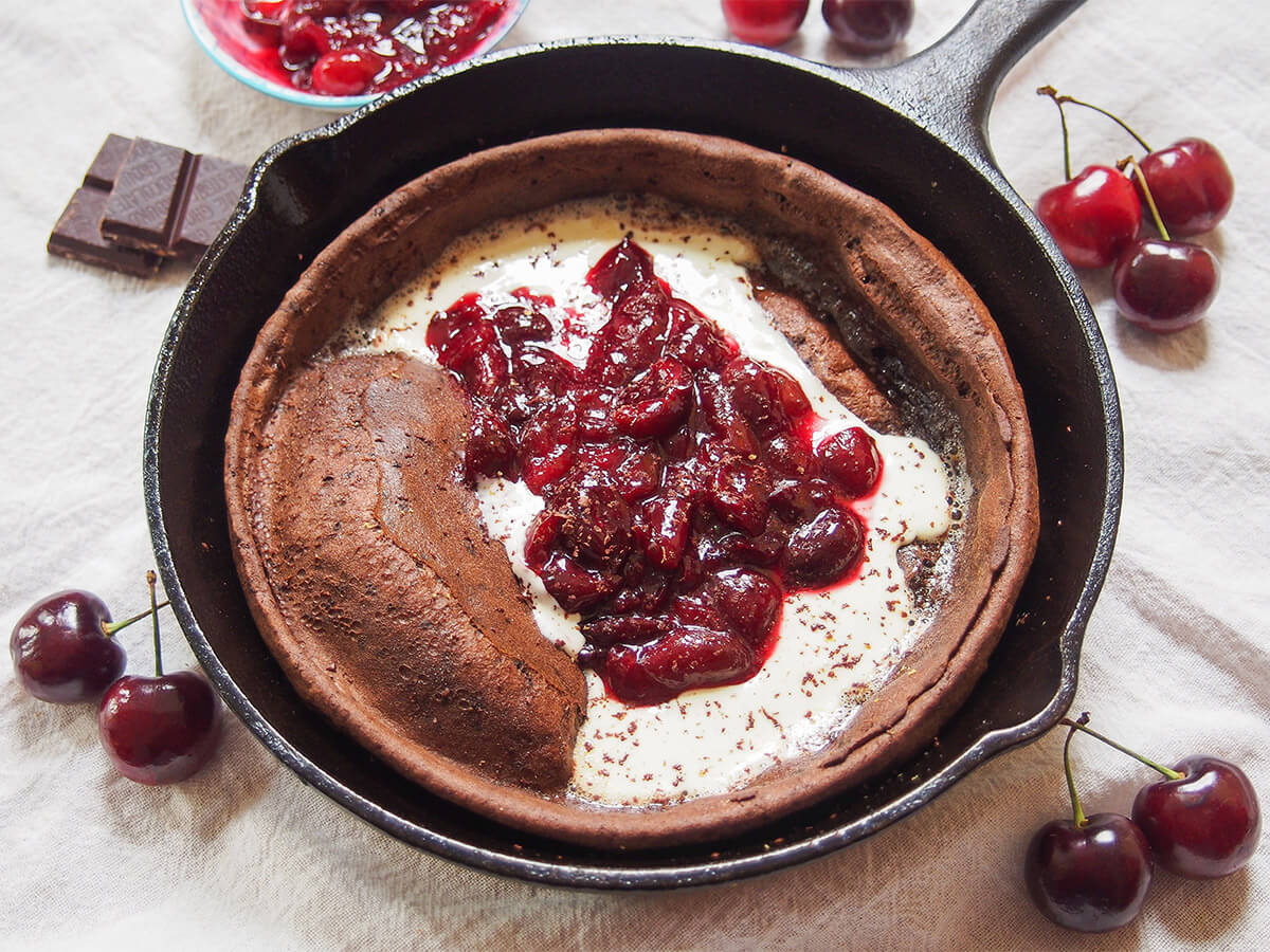 This chocolate Dutch baby pancake with cherry compote is like a breakfast take on black forest cherry cake. It's a deliciously indulgent combination, but best of all, it's actually really easy to make. Perfect for breakfast or dessert! skillet with chocolate Dutch baby pancake topped with cherry compote