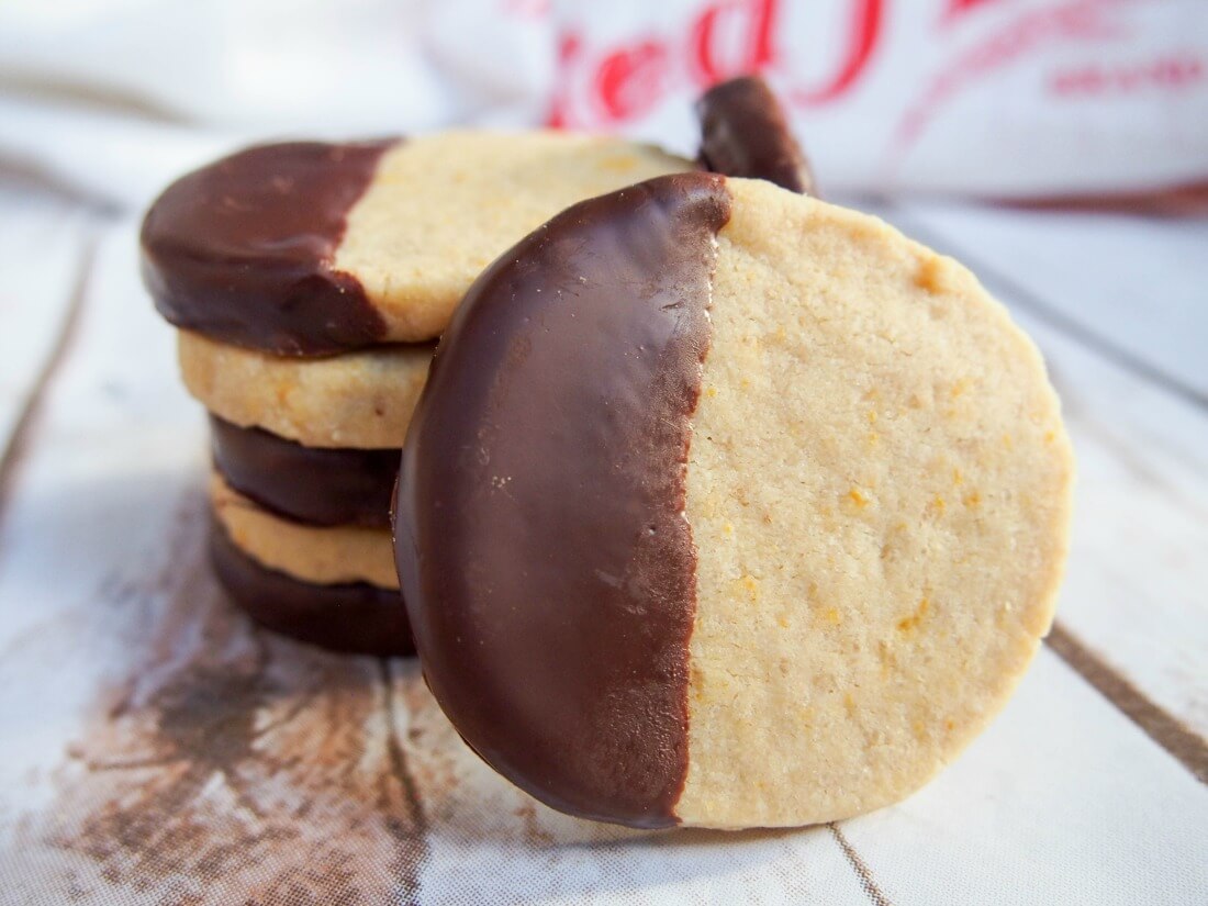 These chocolate orange shortbread cookies are a delicious, festive twist on traditional shortbread. These cookies have fantastic flavors that everyone will love - you'll be making them on repeat. chocolate orange shortbread cookies with one at front resting against stack