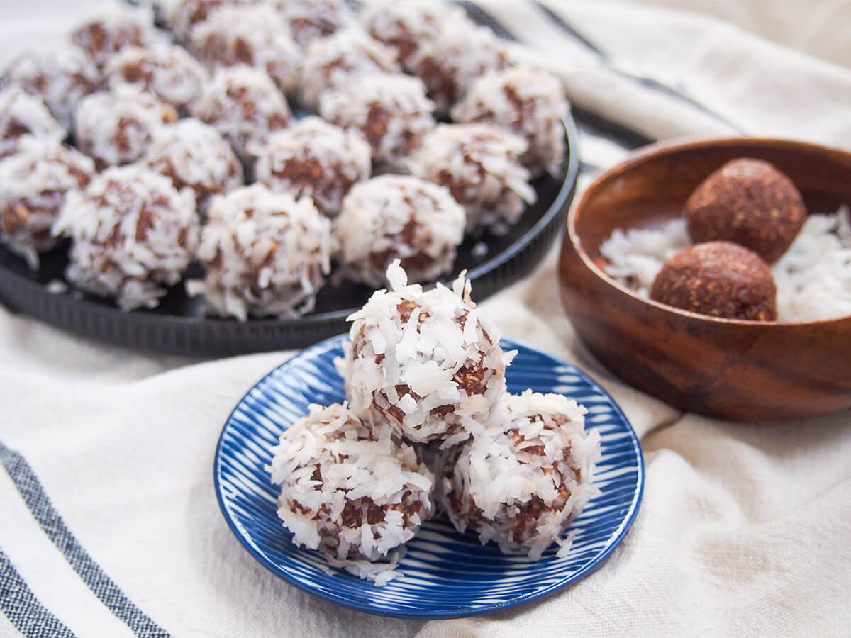 chokladbollar - Swedish chocolate oat balls small stack of chokladbollar with plate of the chocolate oat balls behind