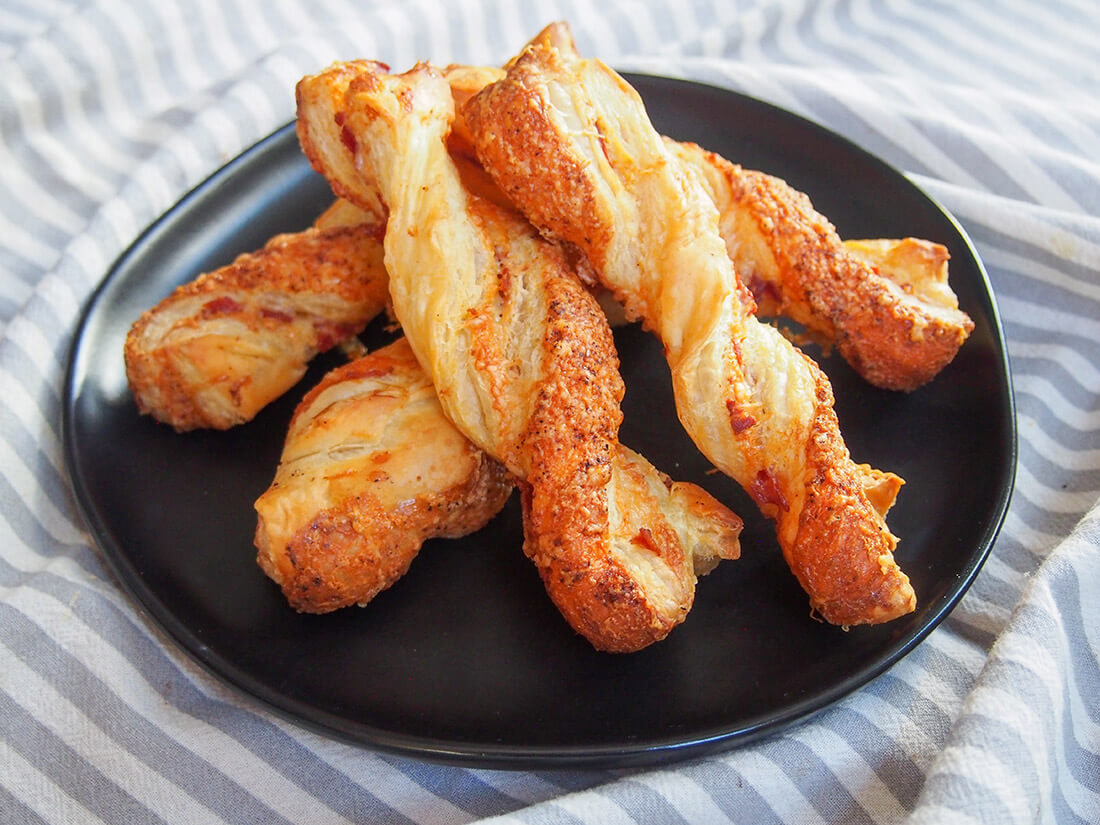 These chorizo cheese twists are incredibly easy to make with just a few ingredients and minimal prep. Then wait just a few minutes before you get to enjoy these addictively tasty, crispy snacks! plate of chorizo cheese twists stacked in middle