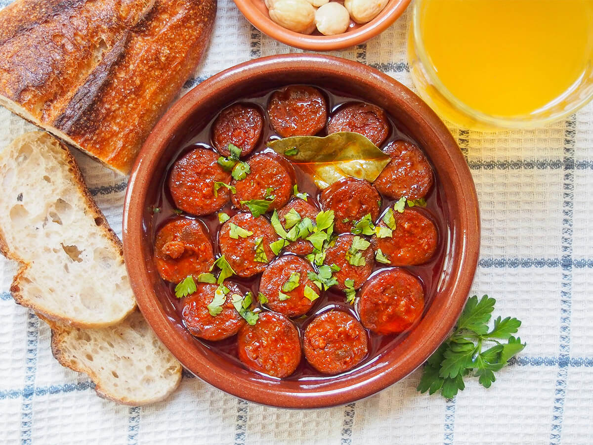 Chorizo a la sidra (Spanish chorizo in cider) dish of chorizo a la sidra (chorizo in cider) with bread to one side and cider to other