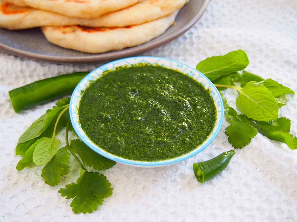 This cilantro mint chutney is the classic Indian "green chutney" that you'll find served in restaurants alongside appetizers and more. It's easy to make, versatile and with a bright, fresh flavor. bowl of cilantro mint chutney with herbs and chili to side of bowl