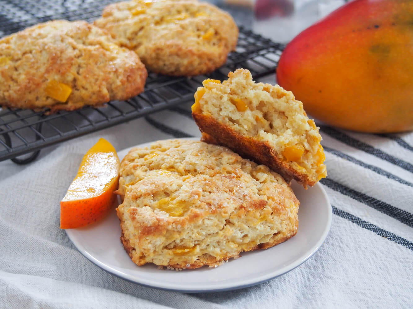 Bite into a taste of the tropics with these delicious coconut mango scones. They're tender inside and crisp outside, packed with juicy fruit and easy to make too. Perfect with your morning coffee, or any excuse. Coconut mango scones with one whole and one split on plate