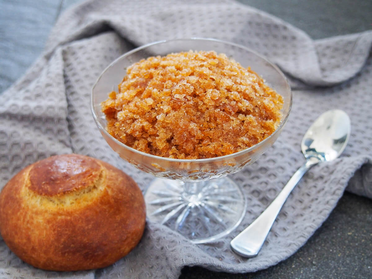 Do like the Sicilians do, and enjoy your coffee in frozen form! This coffee granita is a wonderful combination of sweetened coffee flavors and icy coldness. It's refreshing and delicious. glass of coffee granita with brioche to one side and spoon to other