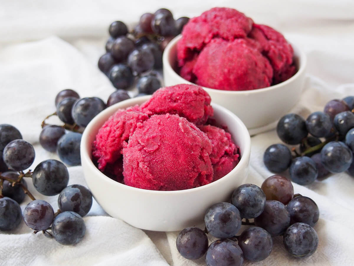 bowls of Concord grape sorbet bowl of Concord grape sorbet with second bowl behind and grapes around bowls.