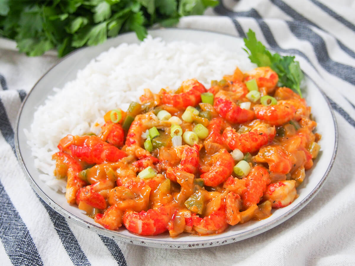 Crawfish etouffee is a classic Cajun stew - this version is lightened up & speeded up a little but still full of fantastic flavors. A comforting seafood stew, it's a delicious dinner whether as part of Mardi Gras celebrations or any time. plate with crawfish etouffee at front and rice behind.