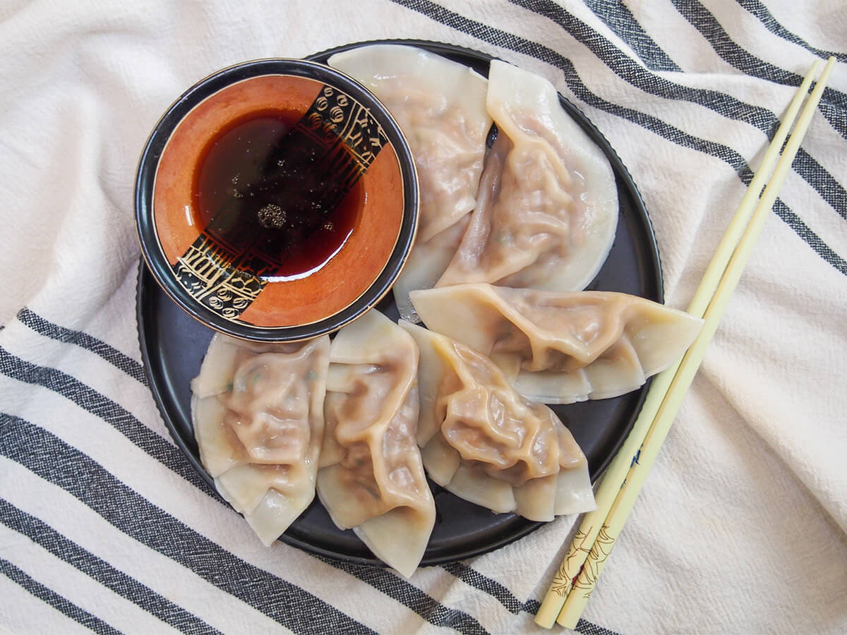 These cumin lamb dumplings are made with lamb and vegetables, and include a touch of cumin which adds a warm spice flavor. They're comforting, incredibly flavorful and most definitely worth trying soon. overhead view of plate of cumin lamb dumplings with chopsticks to side