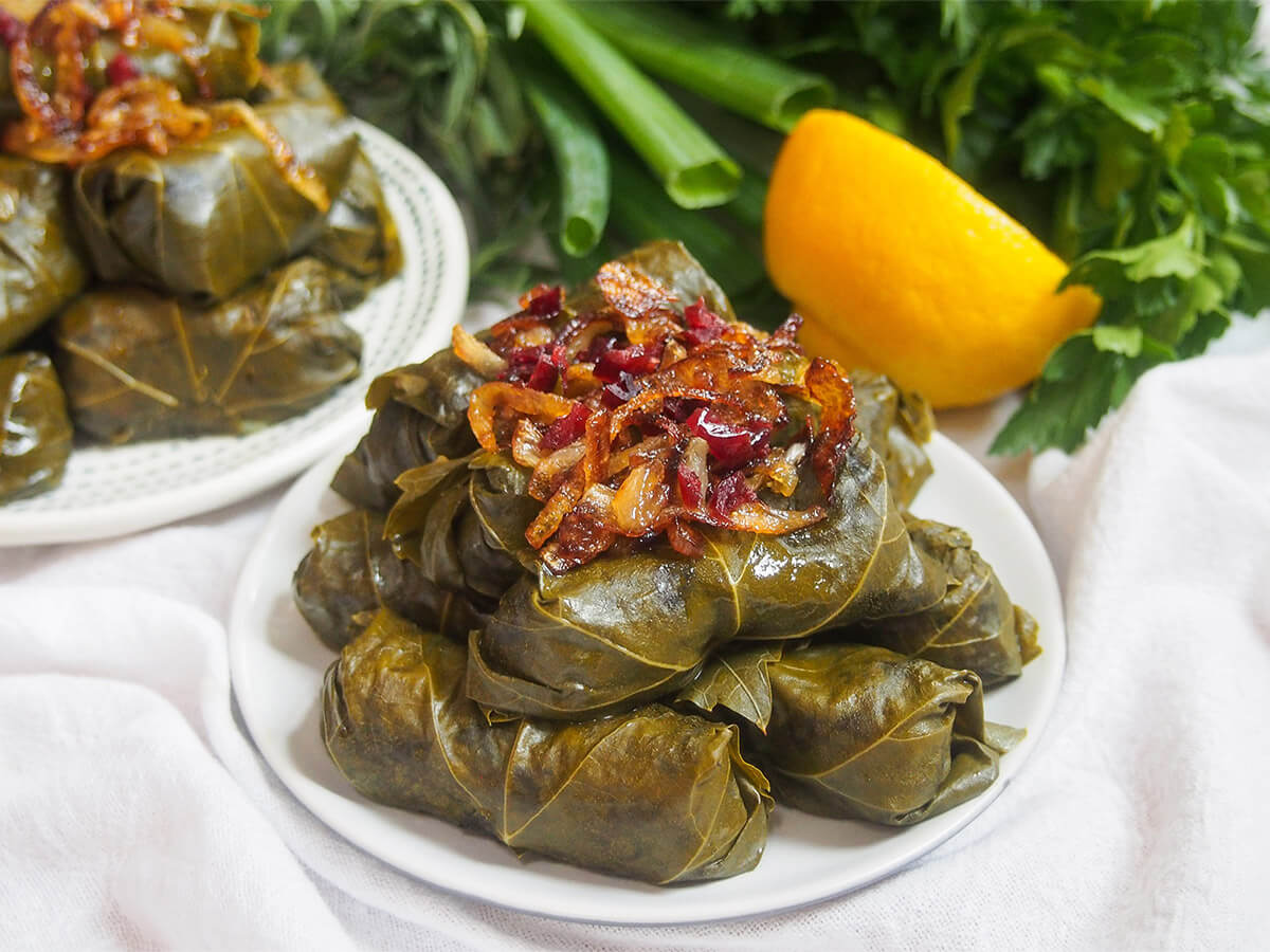 Dolme barge mo are the Persian version of stuffed grape leaves, with a delicious filling of rice, yellow split peas, herbs and meat. They make a great appetizer and work well with other small plates. plate of dolmeh barge mo Persian stuffed grape leaves with second plate and herbs behind