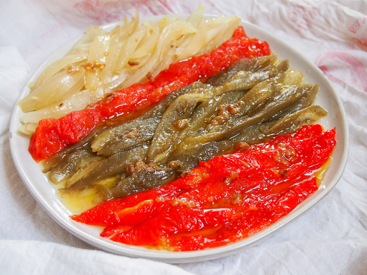 Escalivada is a simple and delicious Catalan side or tapas dish of grilled or roasted vegetables. You don't need many ingredients and it's easy to make, but the result is so tasty and silky smooth. Perfect on bread, with fish and much more. plate of escalivada Catalan roast vegetables with red peppers at front