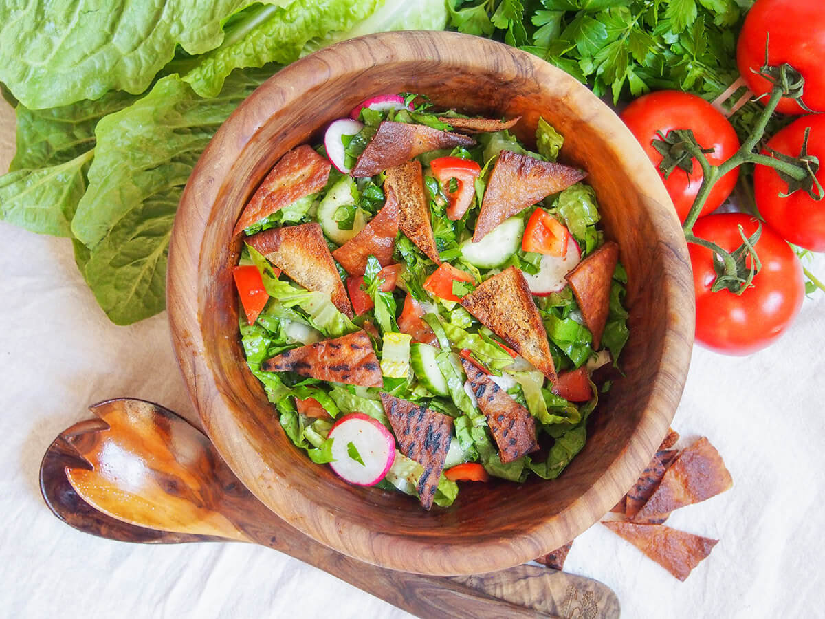 Lebanese fattoush salad is a delicious combination of crunchy vegetables, crisp pita chips and a bright lemon-sumac dressing. It's a Levantine staple for good reason. bowl of fattoush salad from overhead with tomatoes to side and lettuce to other