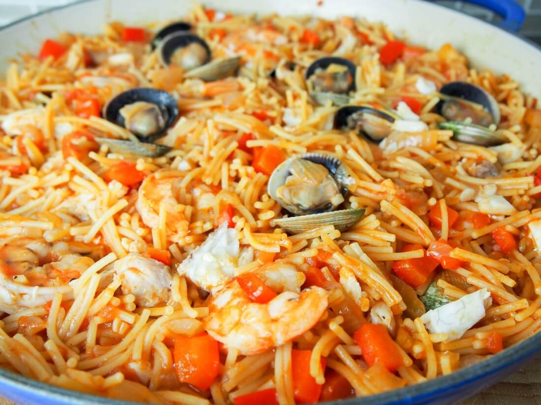 Fideua is a Catalan fish and seafood paella made with short pasta and a tomato-pepper and stock sauce base. Deliciously comforting. fideua (Catalan pasta paella) in pan close up showing clams on top