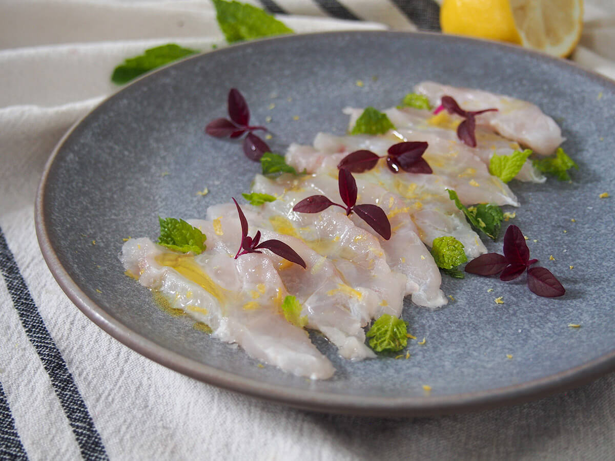 Fish crudo is a simple Italian preparation of raw fish. With only a few ingredients, it takes no time to prepare, but the result is elegant & delicious. plate of fish crudo decorated with microgreens and mint from side