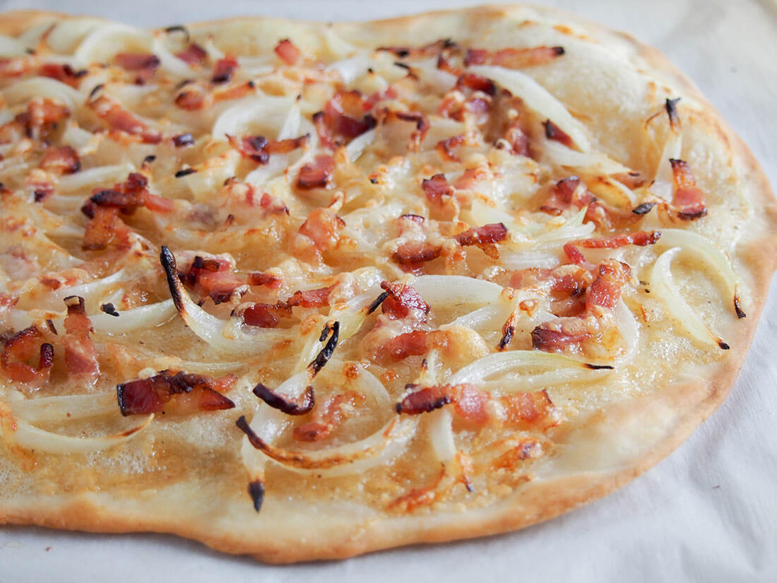 Flammekueche is essentially a bacon onion flatbread/pizza. It may seem like only a few ingredients, but they are transformed into a truly delicious dish you'll instantly love! side view of flammekueche (tarte flambee from Alsace)