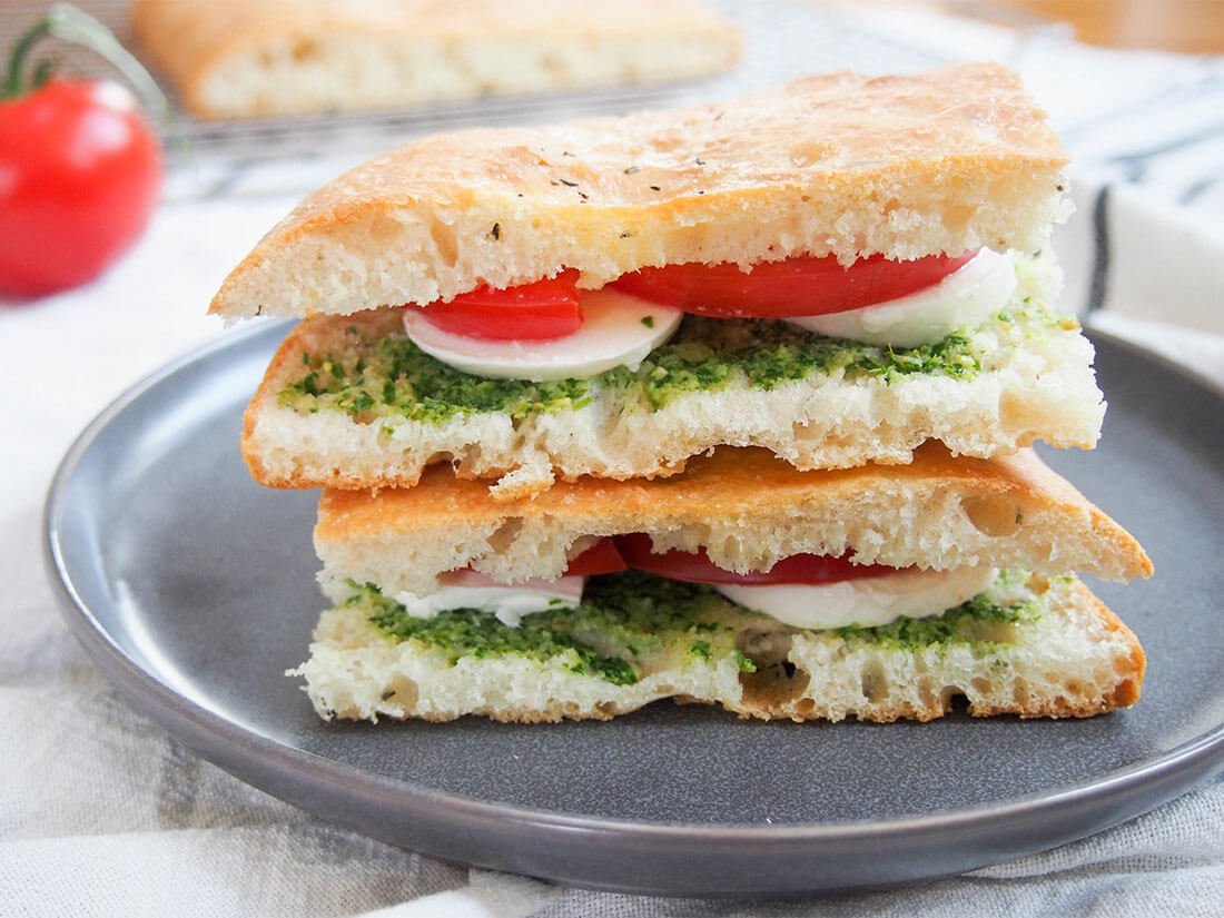 Whether you have homemade or store bought focaccia, it's good for more than just dipping. This caprese focaccia sandwich is incredibly easy and full of bright, fresh flavors. caprese focaccia sandwich on plate with additional bread in background