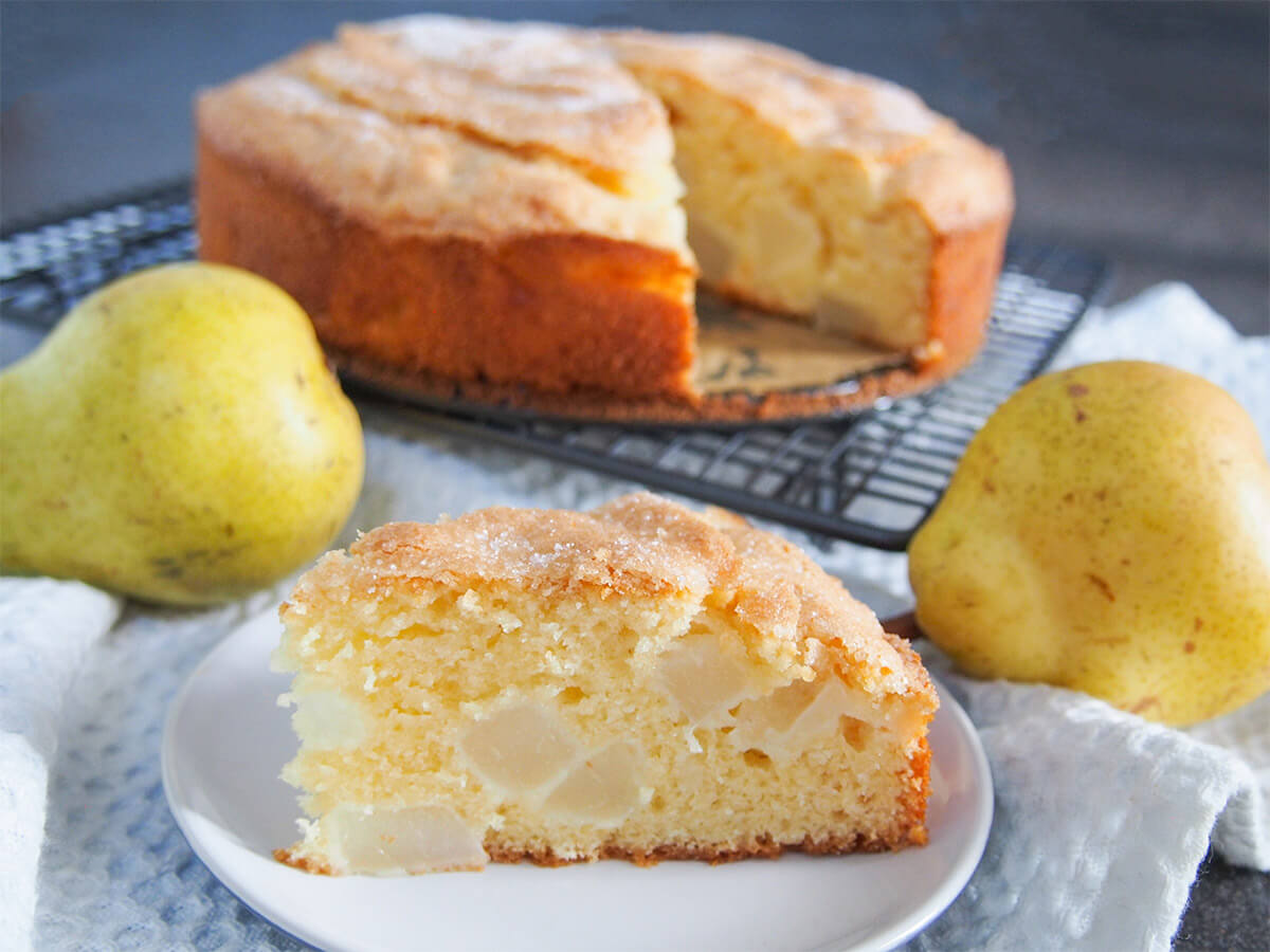 This French-style pear cake is a wonderful combination of tender-crumb cake and juicy chunks of pear. It's easy to make and perfect just as it is for a snack or dressed up for dessert. slice of French pear cake in front of rest of cake with pears to sides
