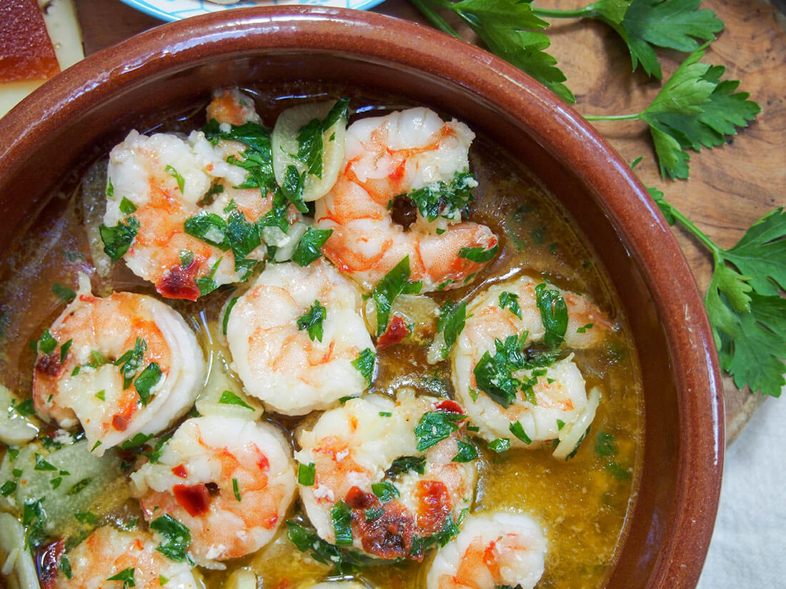Gambas al ajillo are a super simple Spanish tapas that is one of the best known and best loved. And for good reason - these garlic shrimp are delicious! Easy to make and so versatile in how you enjoy them. partial view of dish with gambas al ajillo (Spanish garlic shrimp)