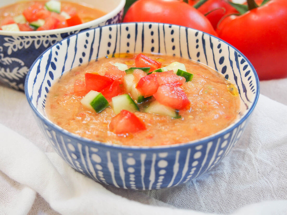 Gazpacho is a classic Spanish cold soup, perfect for summer as an appetizer. It's great for entertaining since it's made ahead. Simple, quick, healthy. bowl of gazpacho garnished with tomato and cucumber