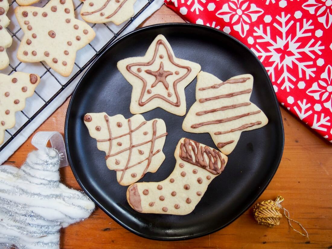 These ginger cookies aren't gingerbread, nor ginger nut cookies, but instead more a ginger-flavored sugar cookie. A traditional German recipe, they're easy and truly delicious. black plate with four German ginger cookies with others on rack to side, and some Christmas decorations on other sides