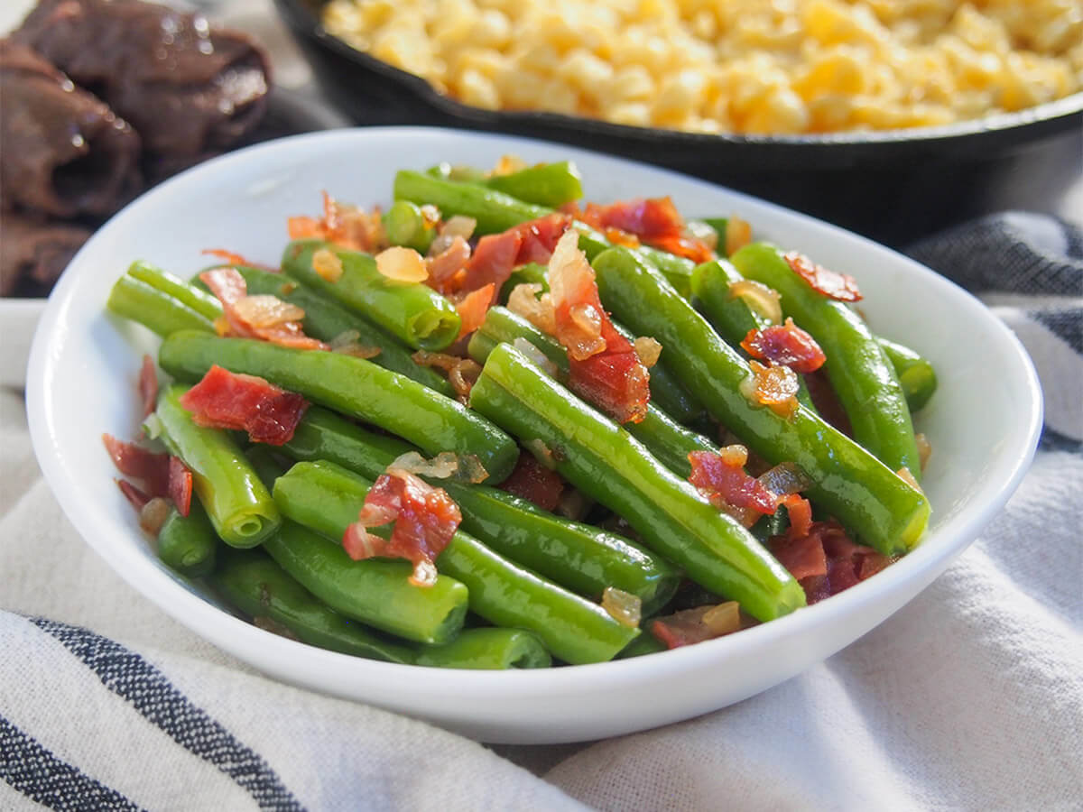 You'd be surprised how a couple of simple additions brighten up plain beans, but that's exactly the case with these speckbohnen, German green beans. These bacony beans make a tasty side, great with lots of mains. side view of bowl of German green beans Speckbohnen