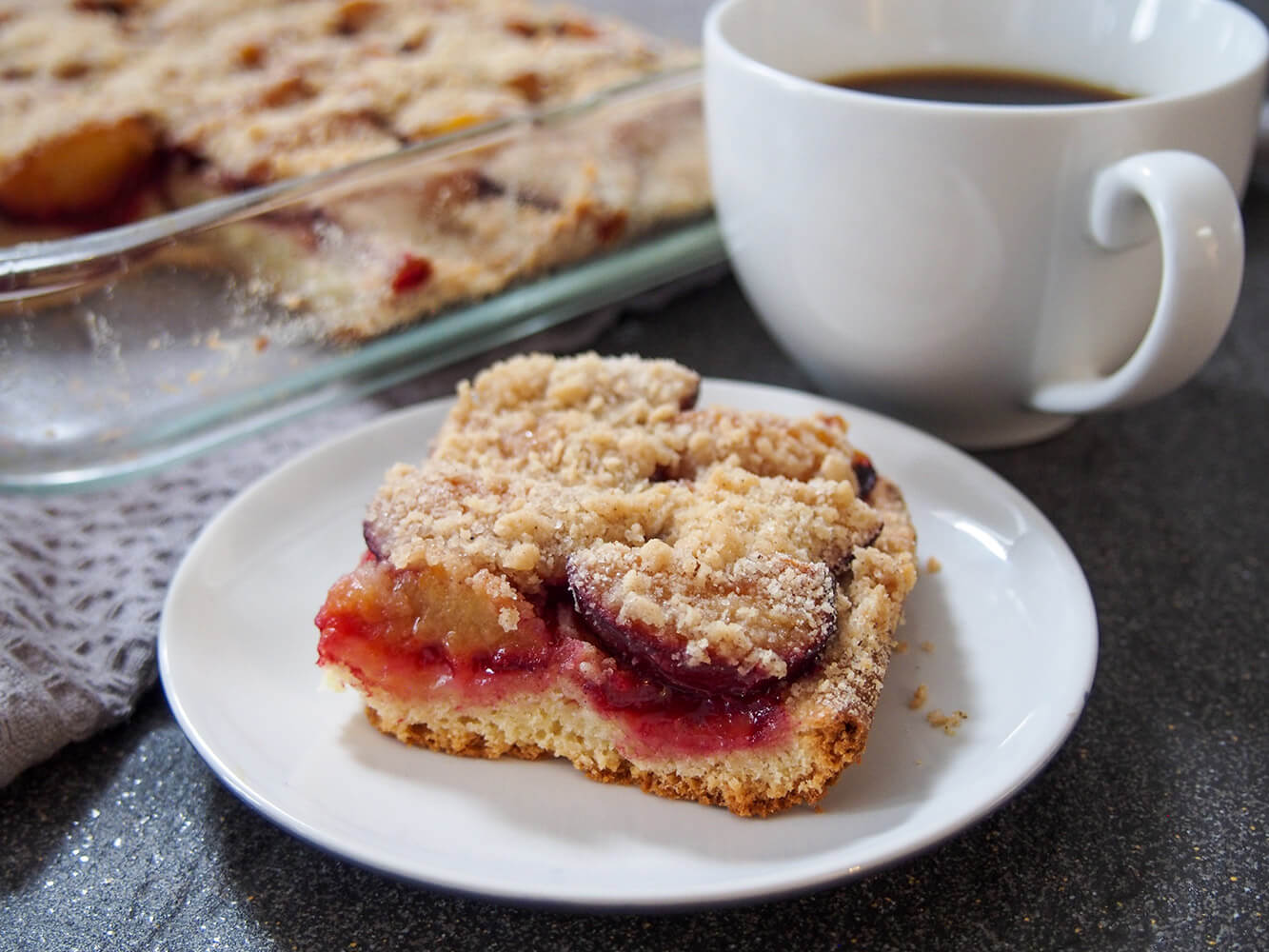 This plum cake is a German classic for "kaffee und kuchen" ie coffee time. It's easy to make and really lets the juicy, sweet-tart plum flavor shine. slice of German plum cake (pflaumenkuchen) with cup of coffee to side