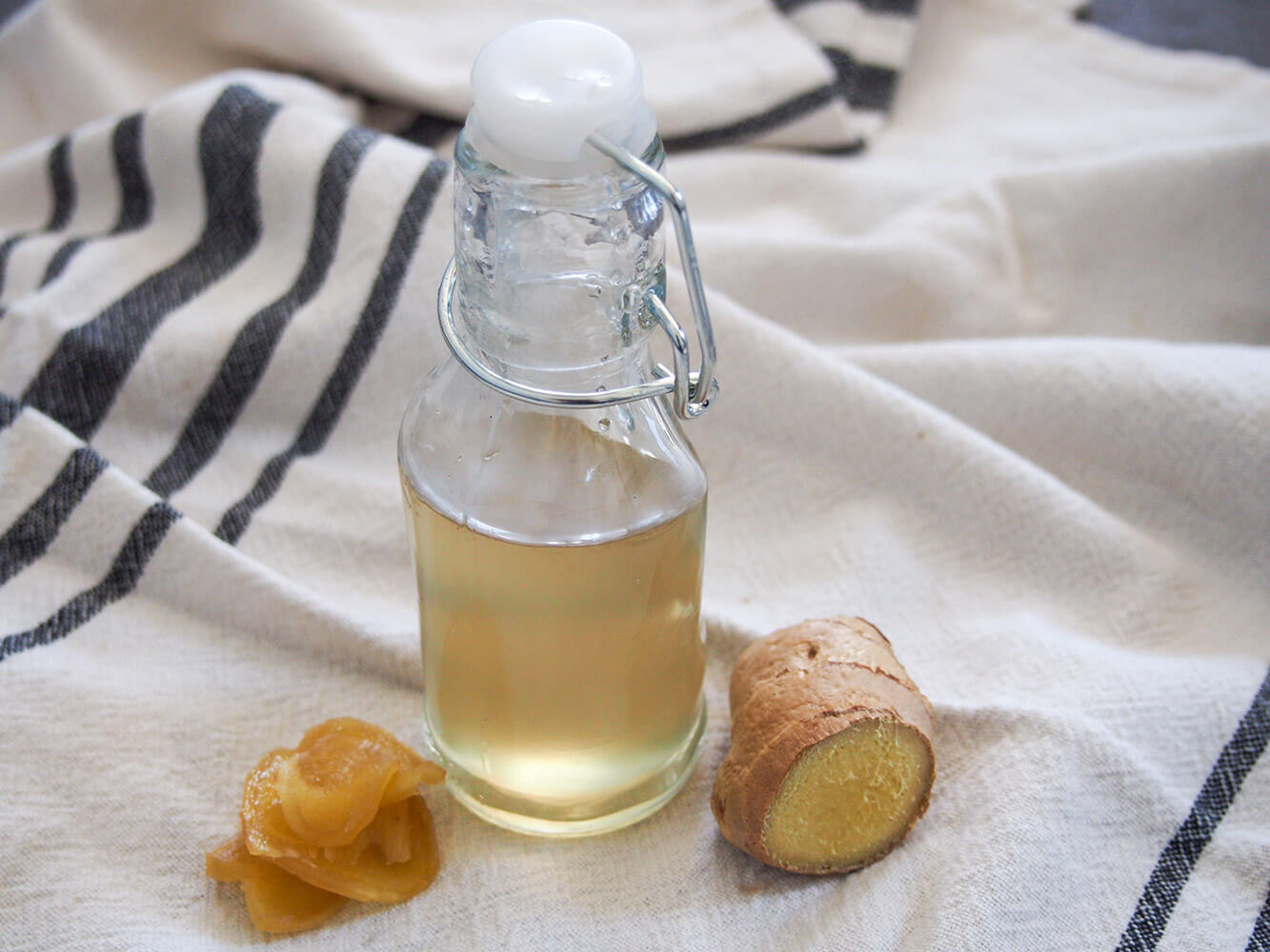 bottle of homemade ginger syrup - a wonderful flavor to add to both cocktails and make non-alcoholic drinks bottle of ginger syrup with piece of fresh ginger to side