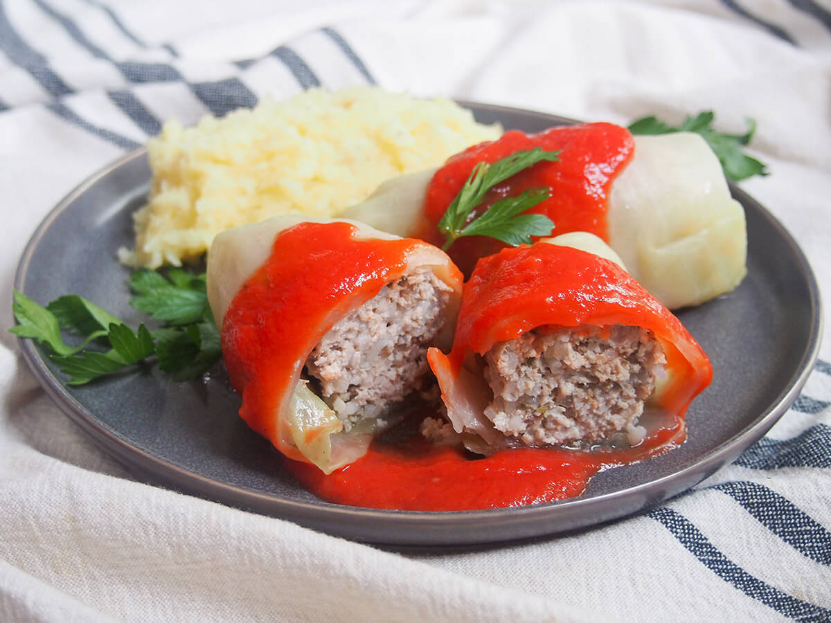 golabki, Polish stuffed cabbage rolls a cut golabki in front of a whole stuffed cabbage roll and mashed potato, sauce over top and parsley garnish.