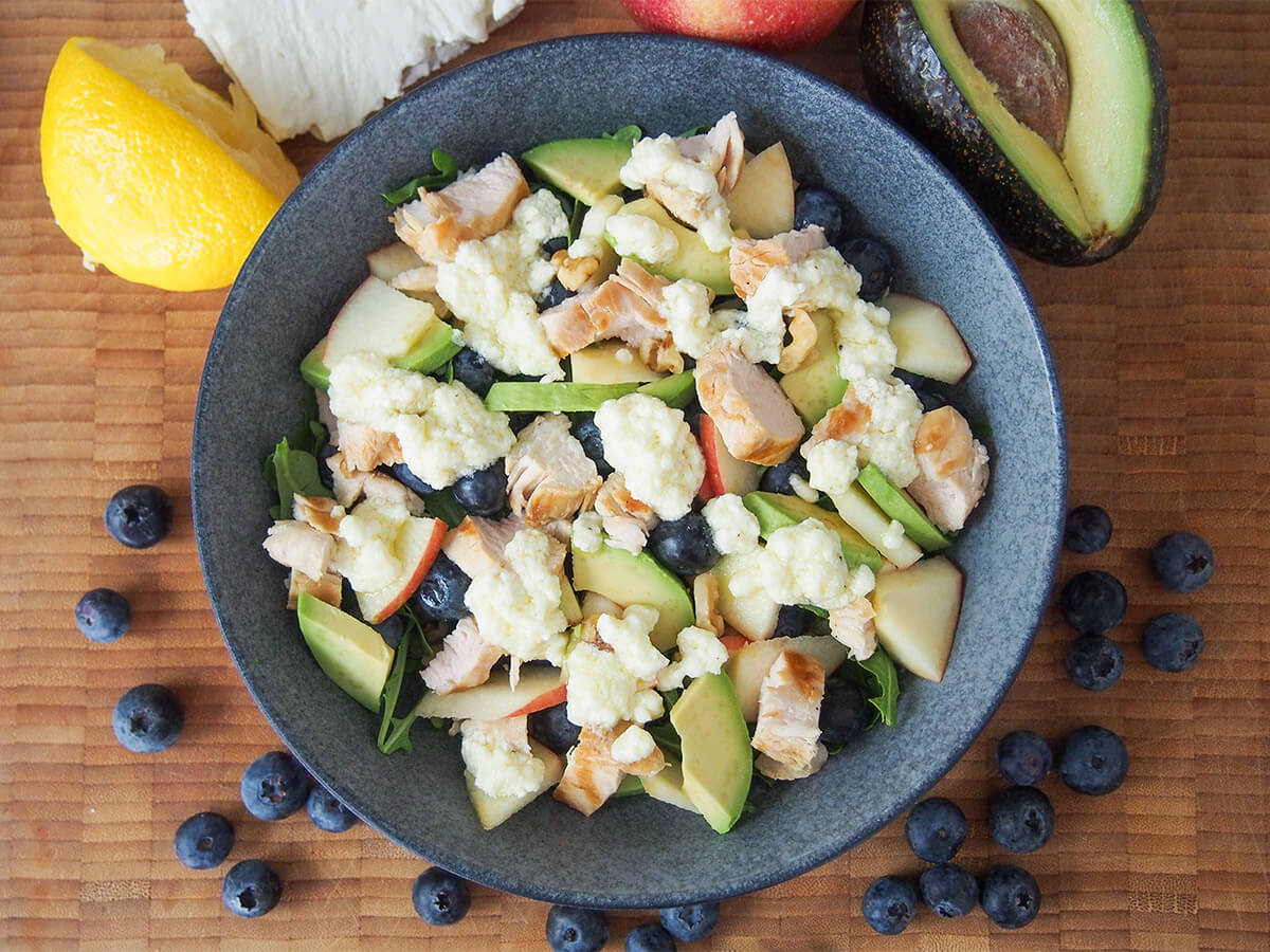 This grilled chicken and blueberry salad is healthy, easy to make & full of delicious flavors from the lemon-feta dressing to berries & nuts. It makes a wonderful lunch, but works any time. bowl of grilled chicken blueberry salad with blueberries around bowl and lemon and avocado above